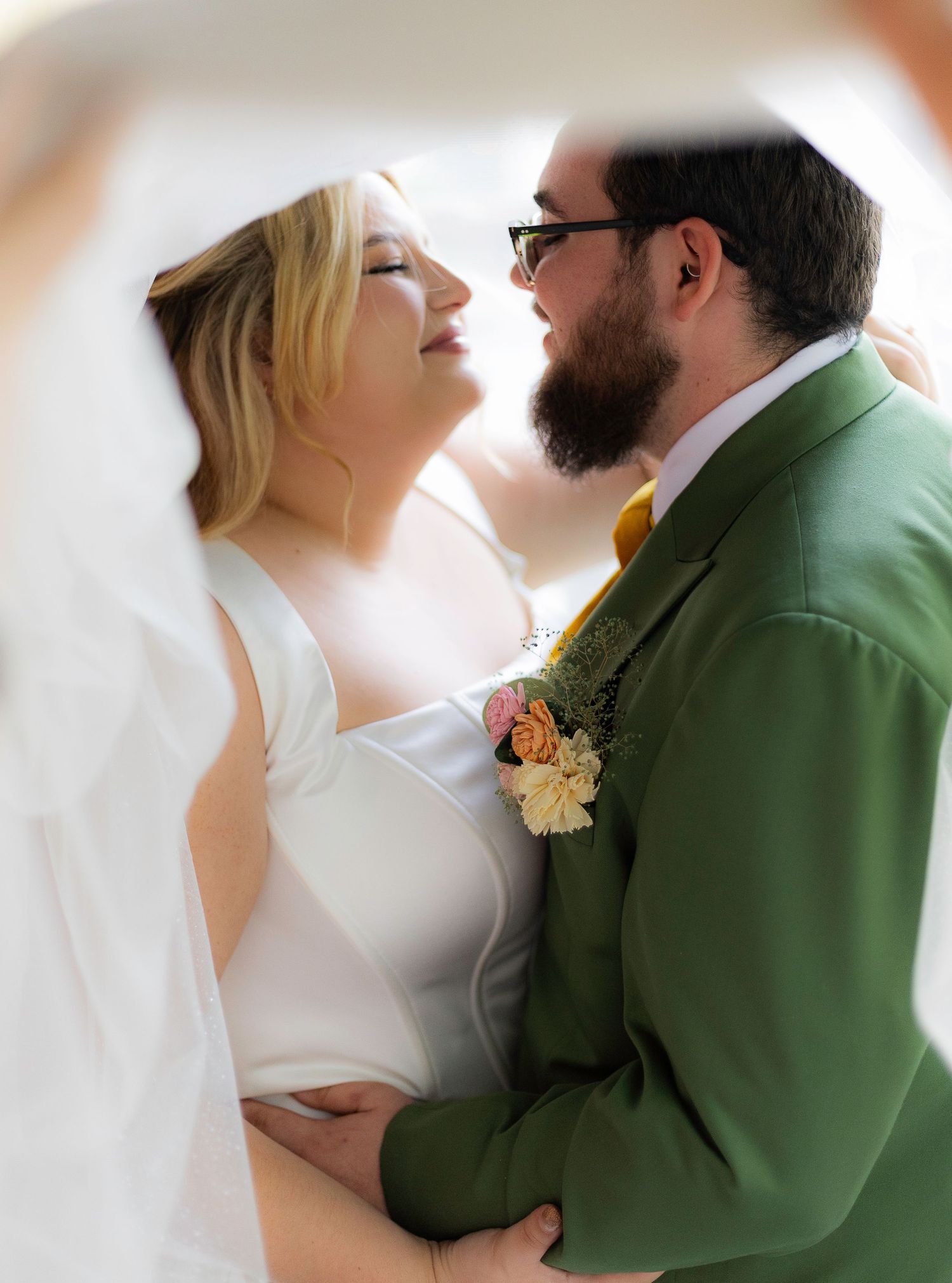 Wedding couple embraces in romantic poses wearing white dress and green suit.