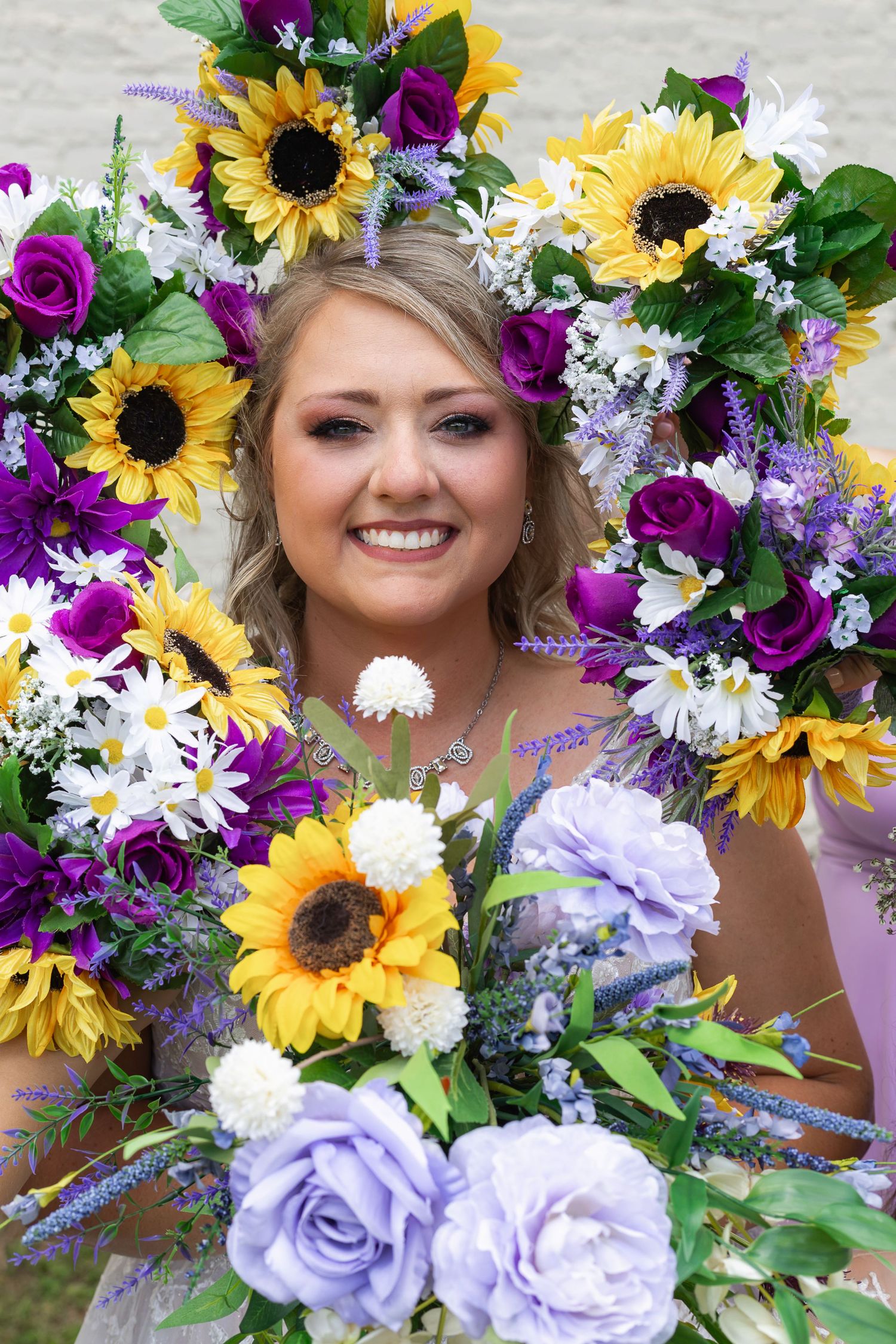 Vibrant wedding bouquet with sunflowers, purple roses, and white daisies against a light background.