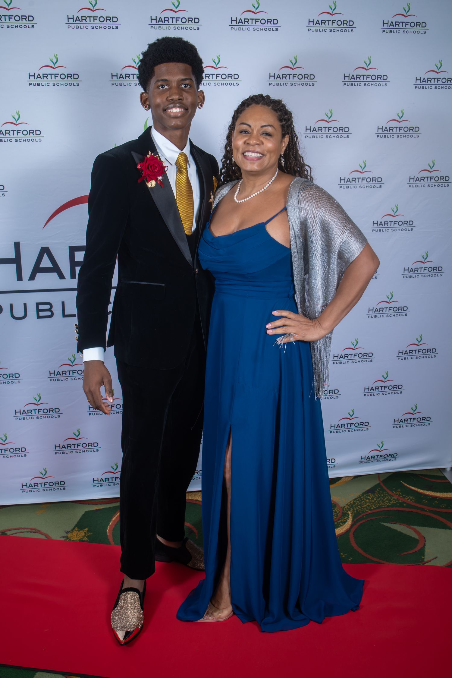 Two students pose on a red carpet at Hartford Public Schools formal event, wearing elegant prom attire.