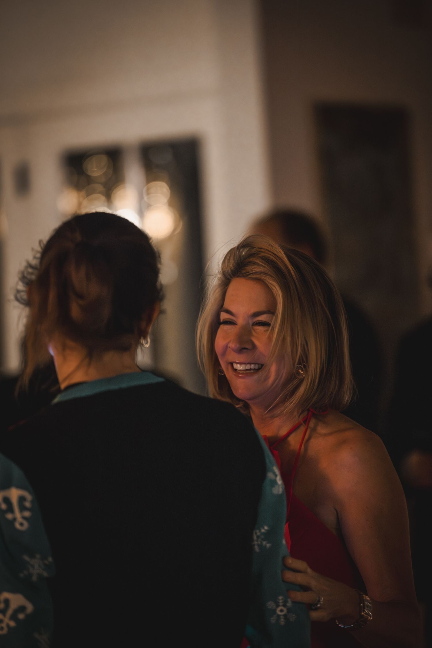 A smiling blonde woman in a red dress socializes at an elegant indoor evening event.