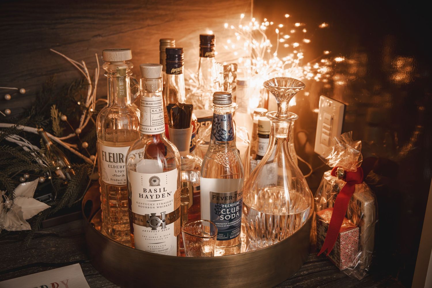 Assorted liquor bottles displayed on a tray with warm fairy lights at a festive bar setup.