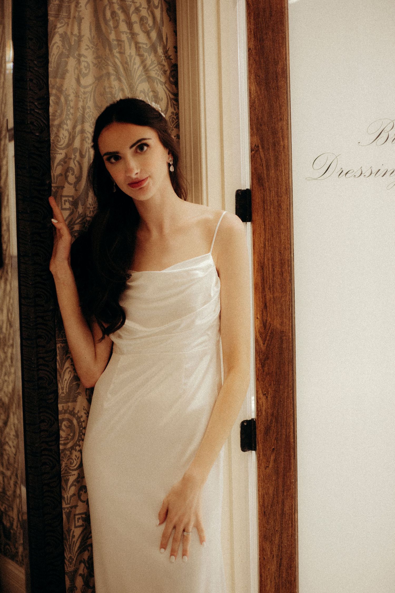 Bride stands draped in soft gold light in her bridal suite.