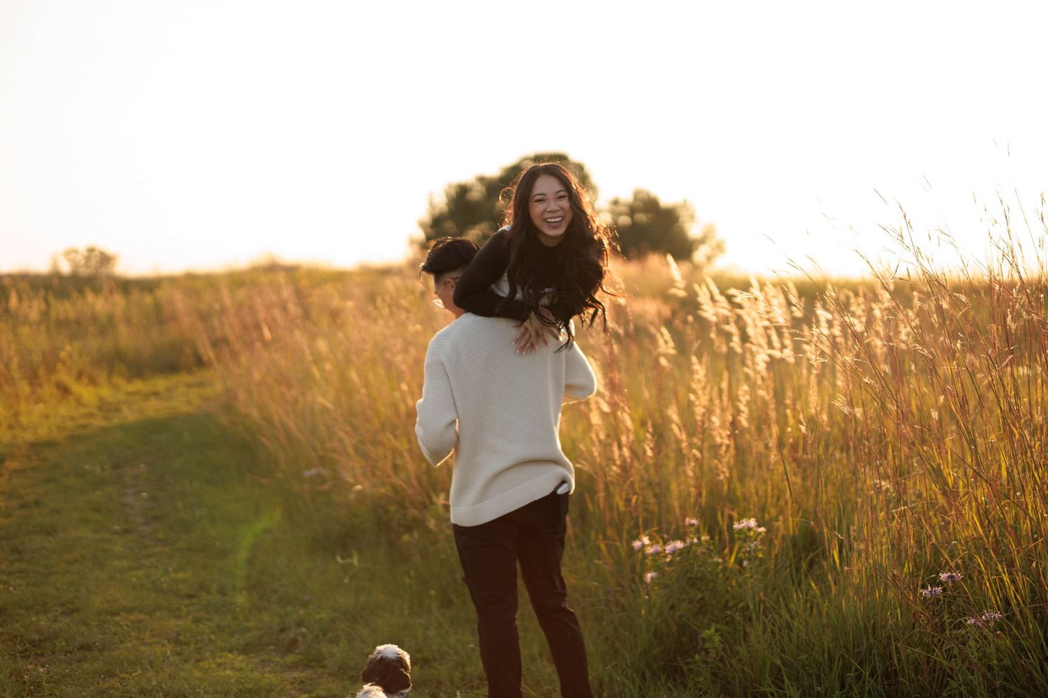 A couple embraces in a golden sunset field, silhouetted against the warm evening light and tall grass.