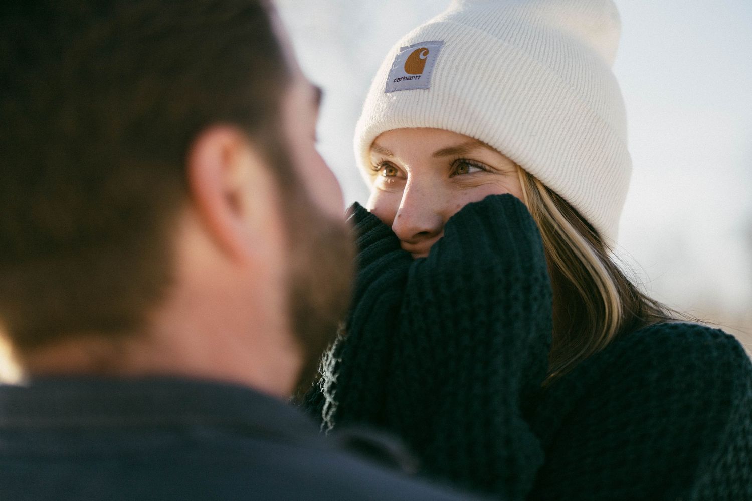 Person wearing a white beanie and black sweater peering over their turtleneck while in conversation.