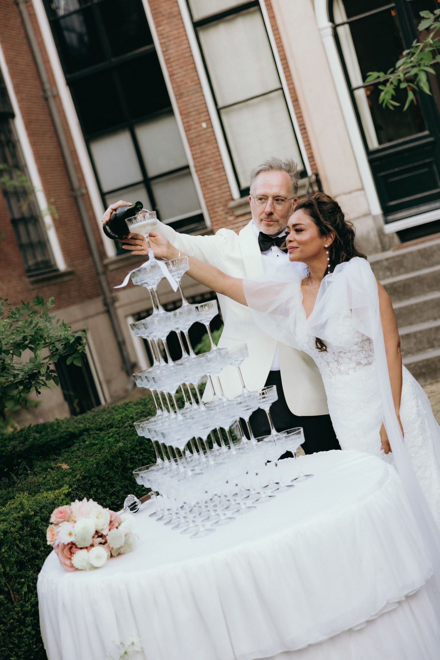 Champagne tower being poured at an elegant outdoor wedding reception.