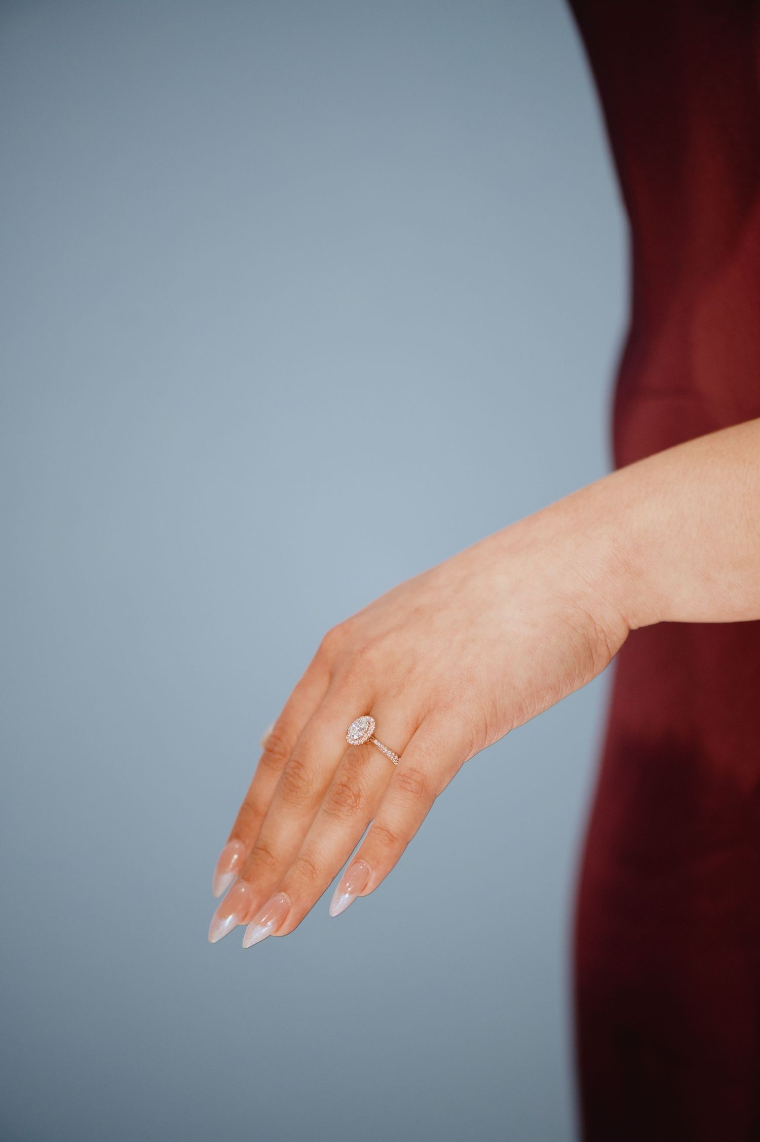 A close-up of a woman's hand wearing a sparkling oval engagement ring with soft white manicured nails.