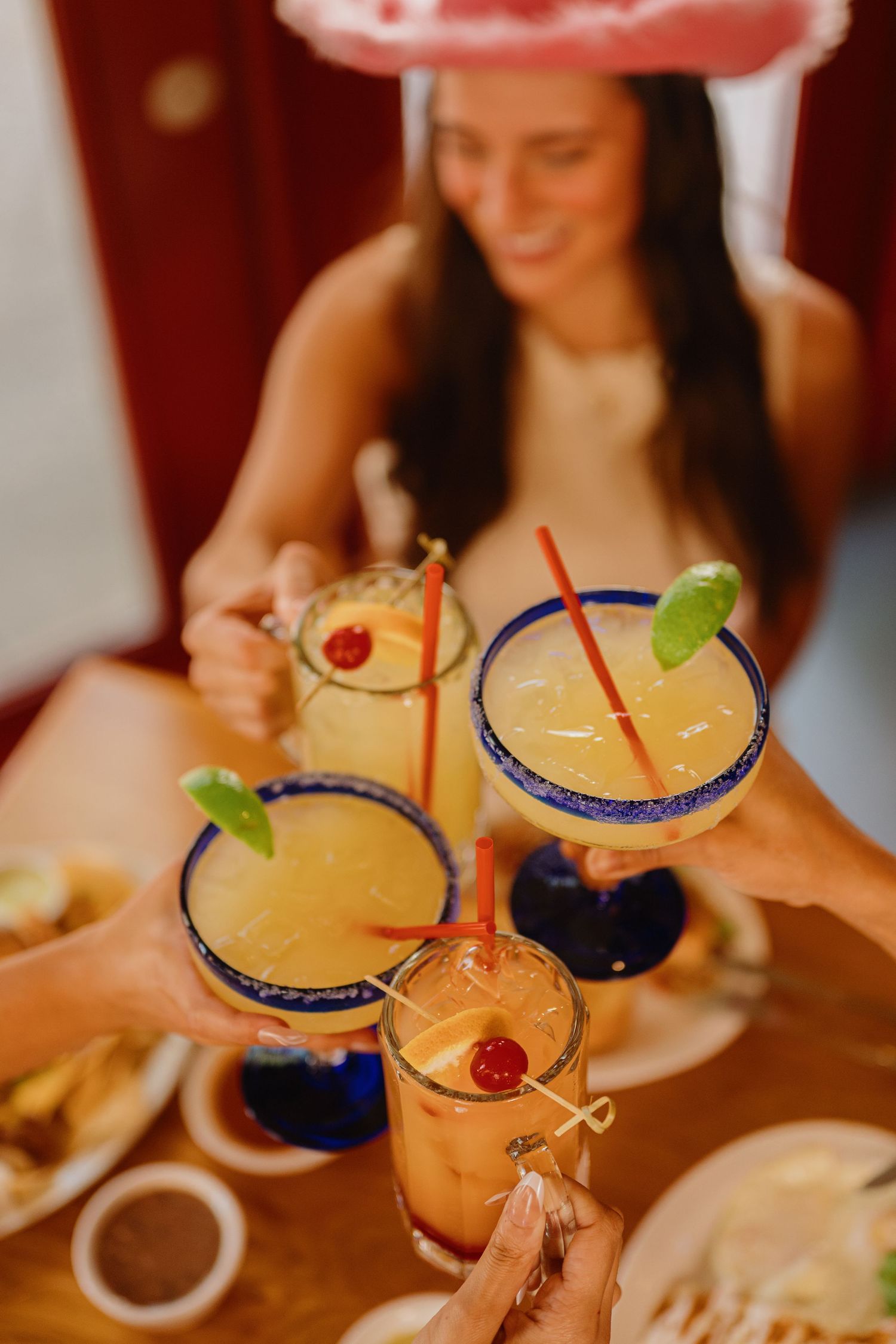 Friends toasting with salt-rimmed margaritas garnished with lime and cherries at a festive restaurant table.