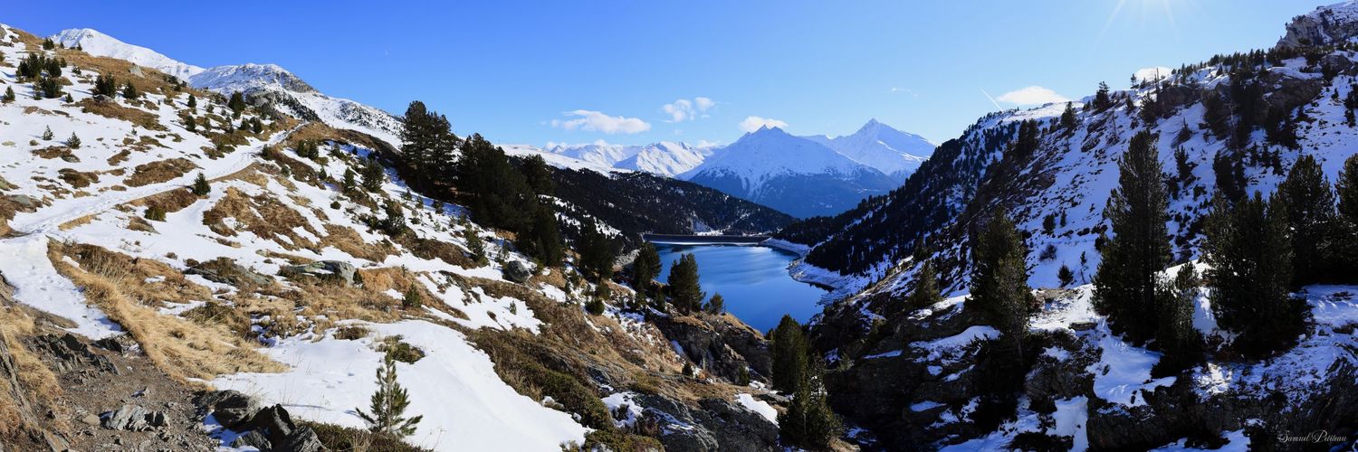 Un lac d'un bleu profond niché au cœur d'une vallée alpine enneigée, encadré par des conifères et des sommets majestueux sous un ciel clair.