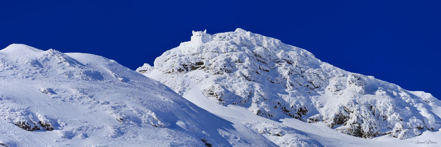 Sommet de montagne enneigé et fort de Ronce immaculé se détachant sur un ciel bleu électrique. Versant d'un blanc pur sous la lumière.