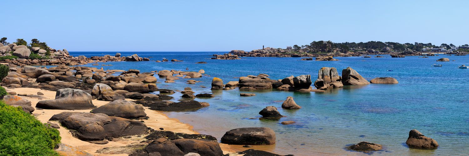 Panorama de la Côte de Granit Rose en Bretagne : rochers polis, plage de sable fin et eau turquoise sous un ciel bleu éclatant.