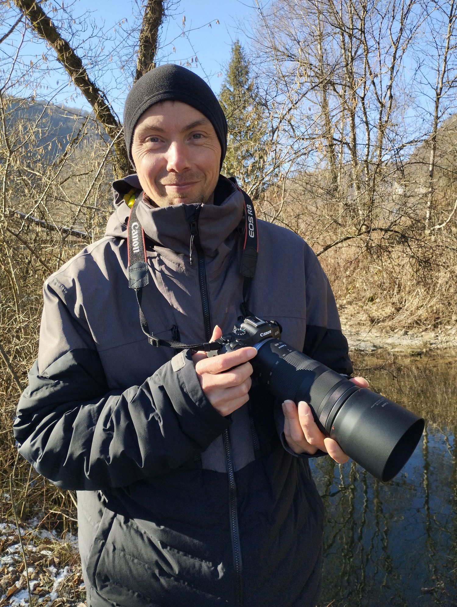 Portrait du photographe Samuel Petiteau en extérieur, portant son équipement professionnel avec un téléobjectif pour la faune sauvage.