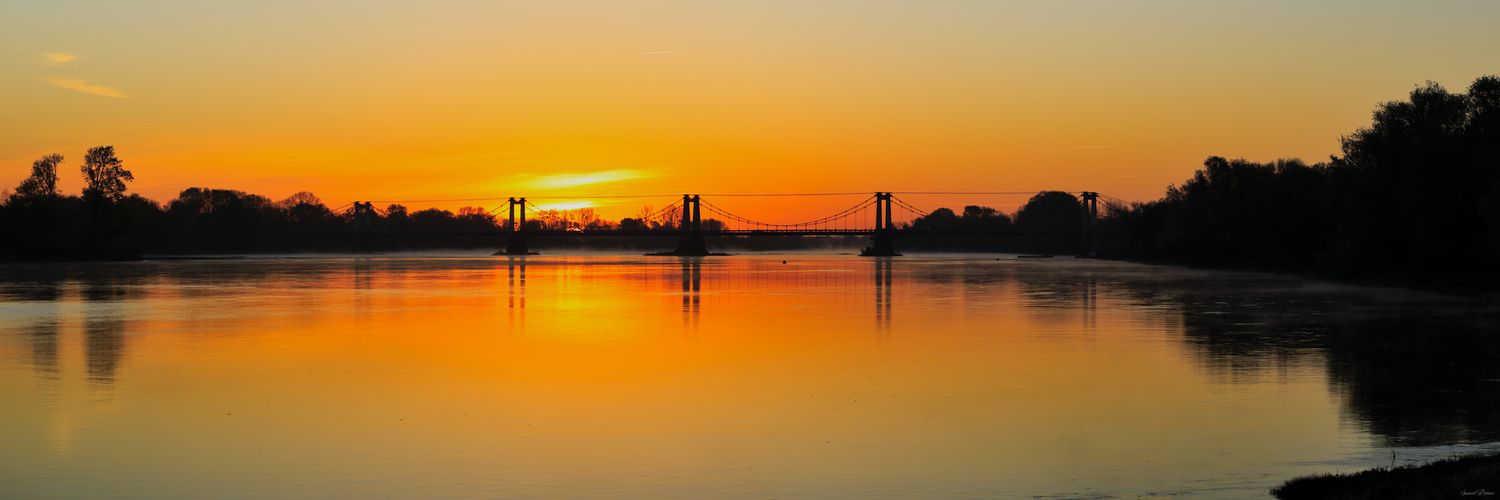 Aurore de feu sur la Loire. Le pont de Montjean se reflète dans une eau d'or, entre brume légère et sérénité pure. Un instant de grâce.