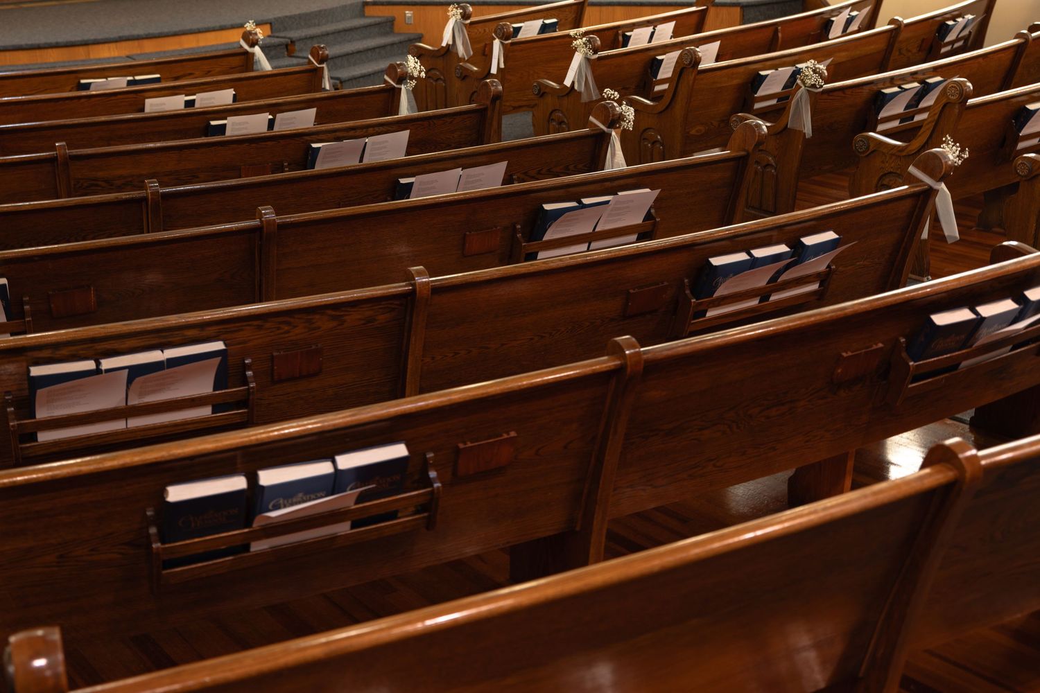 Rows of empty dark wooden church pews with hymnals and songbooks tucked into the backs of the benches inside a quiet sanctuary.