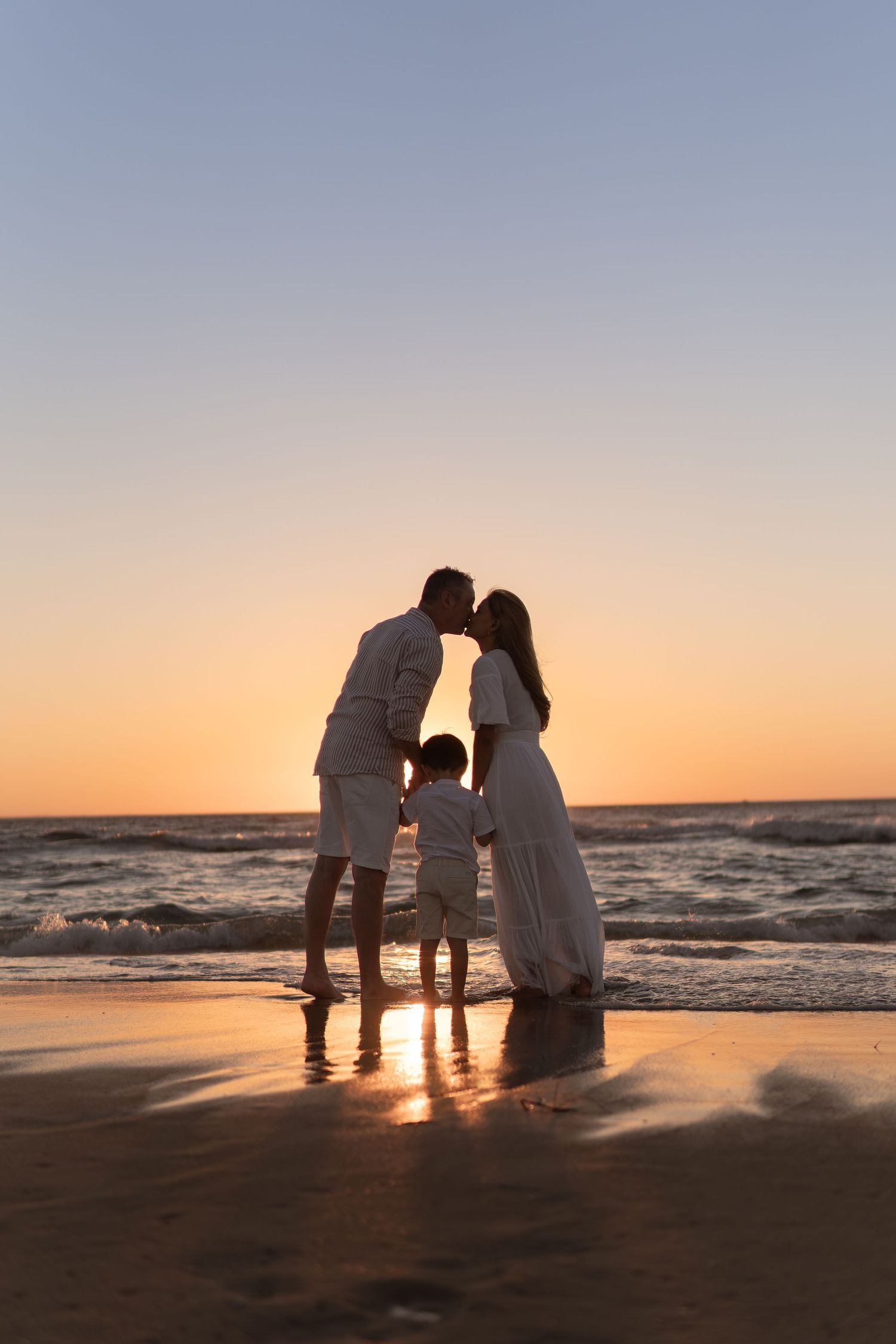 Family silhouettes gather together on beach at sunset with waves rolling in.