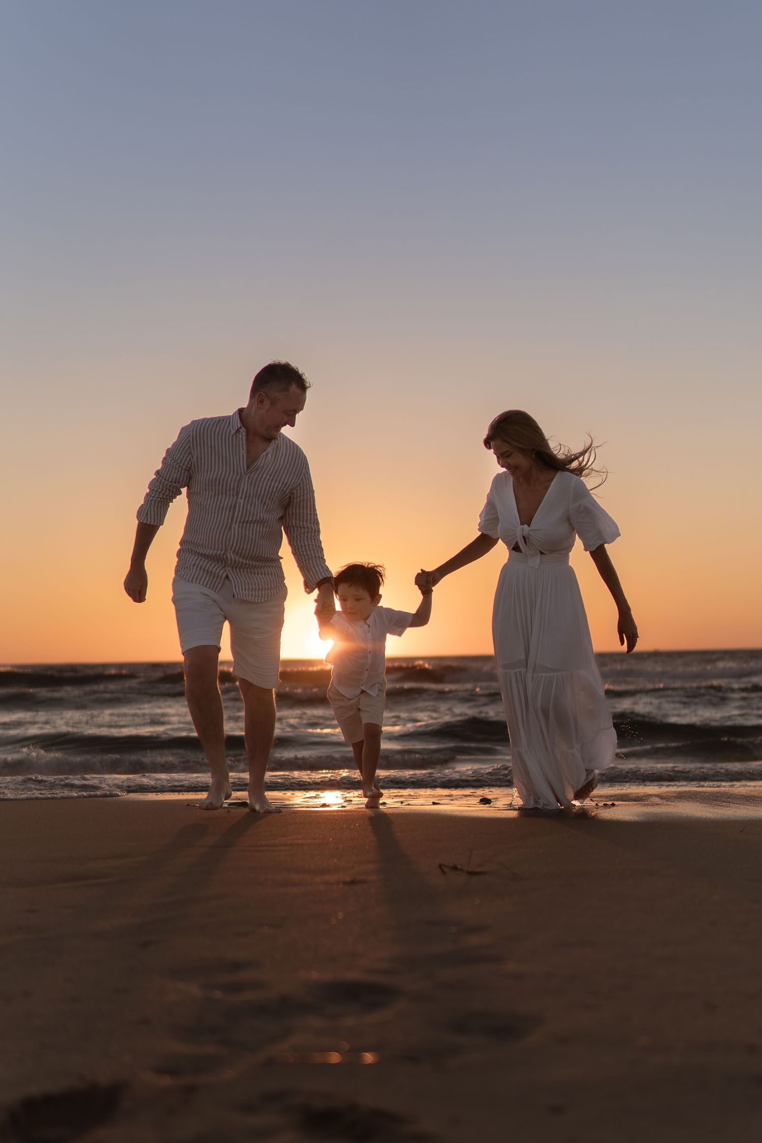 Family members play and interact on beach during sunset with ocean waves in background.