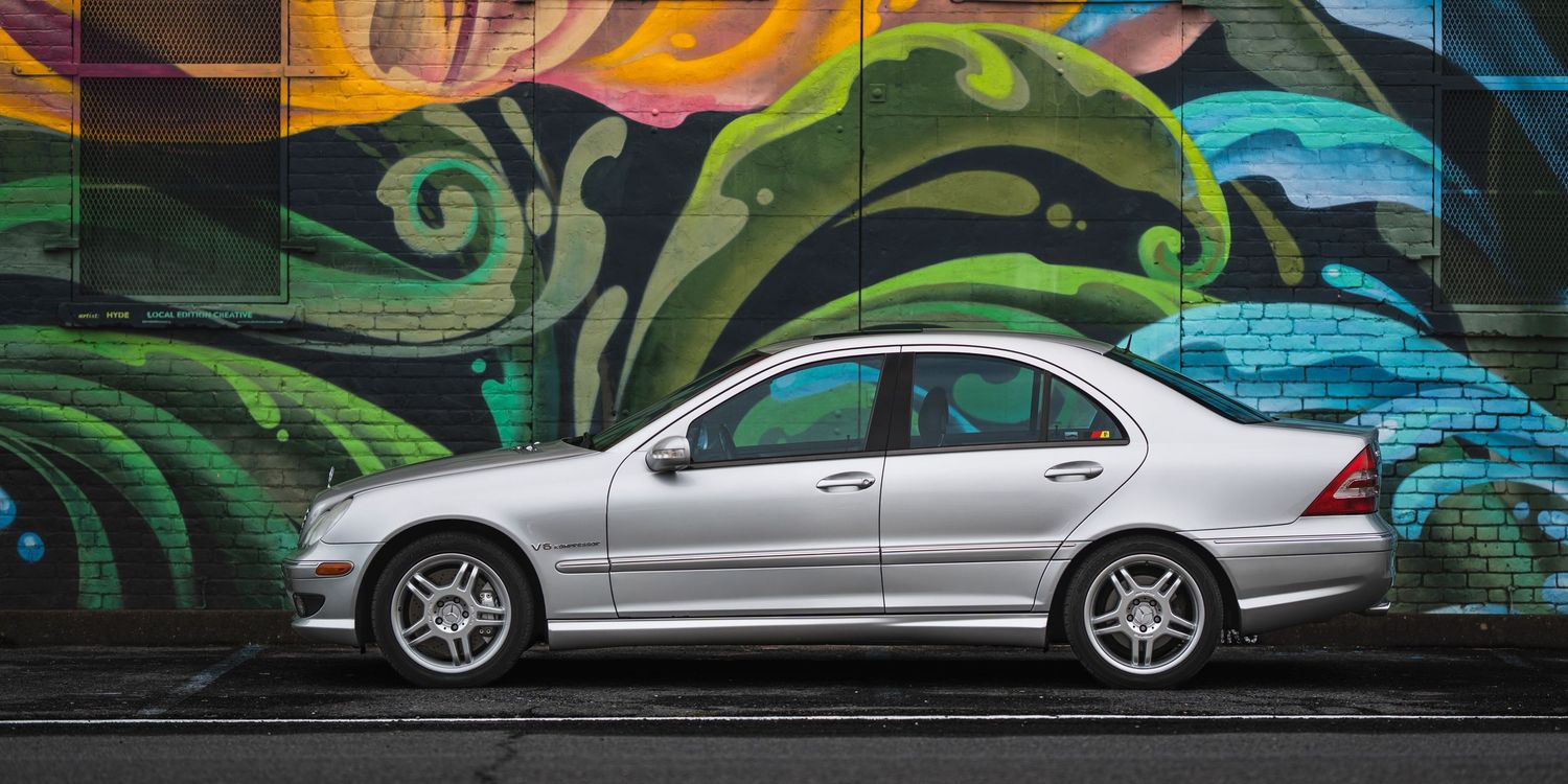 Silver Mercedes-Benz C32 AMG sedan parked in front of a colorful graffiti wall with swirling green and orange designs.