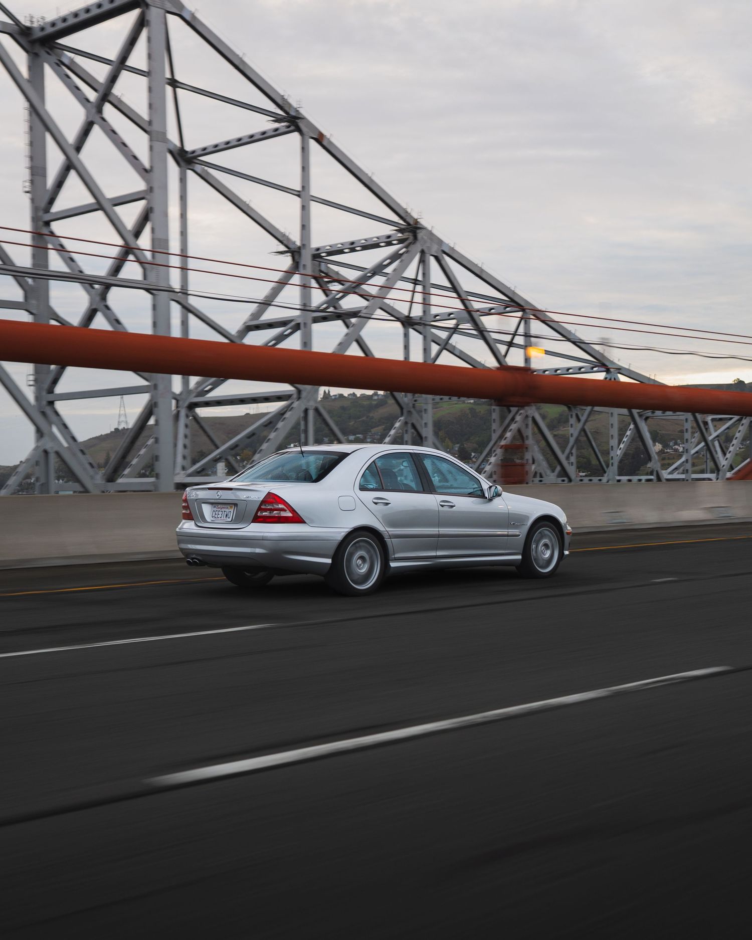 A silver C32 AMG Mercedes-Benz drives across the Alfred Zampa Memori bridge with dramatic architectural elements in the background.
