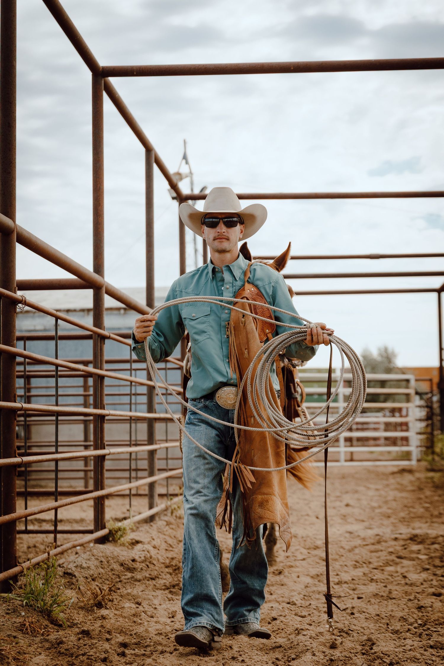 A North Platte, Nebraska lifestyle session cowboy in a corral with a lasso and horse at a stockyard.