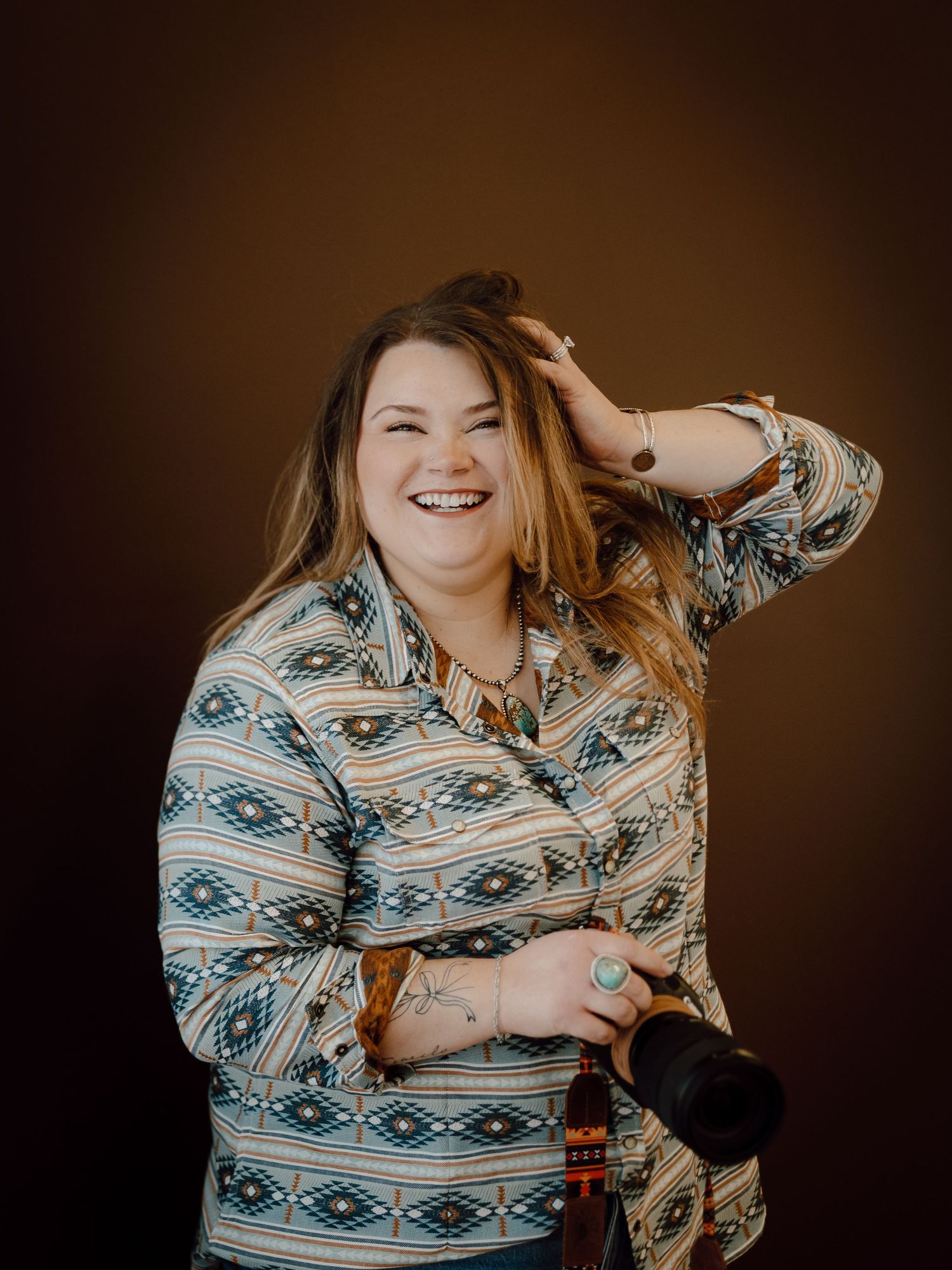 A North Platte lifestyle photographer in a patterned blue and white western style shirt smiles while running fingers through her hair.