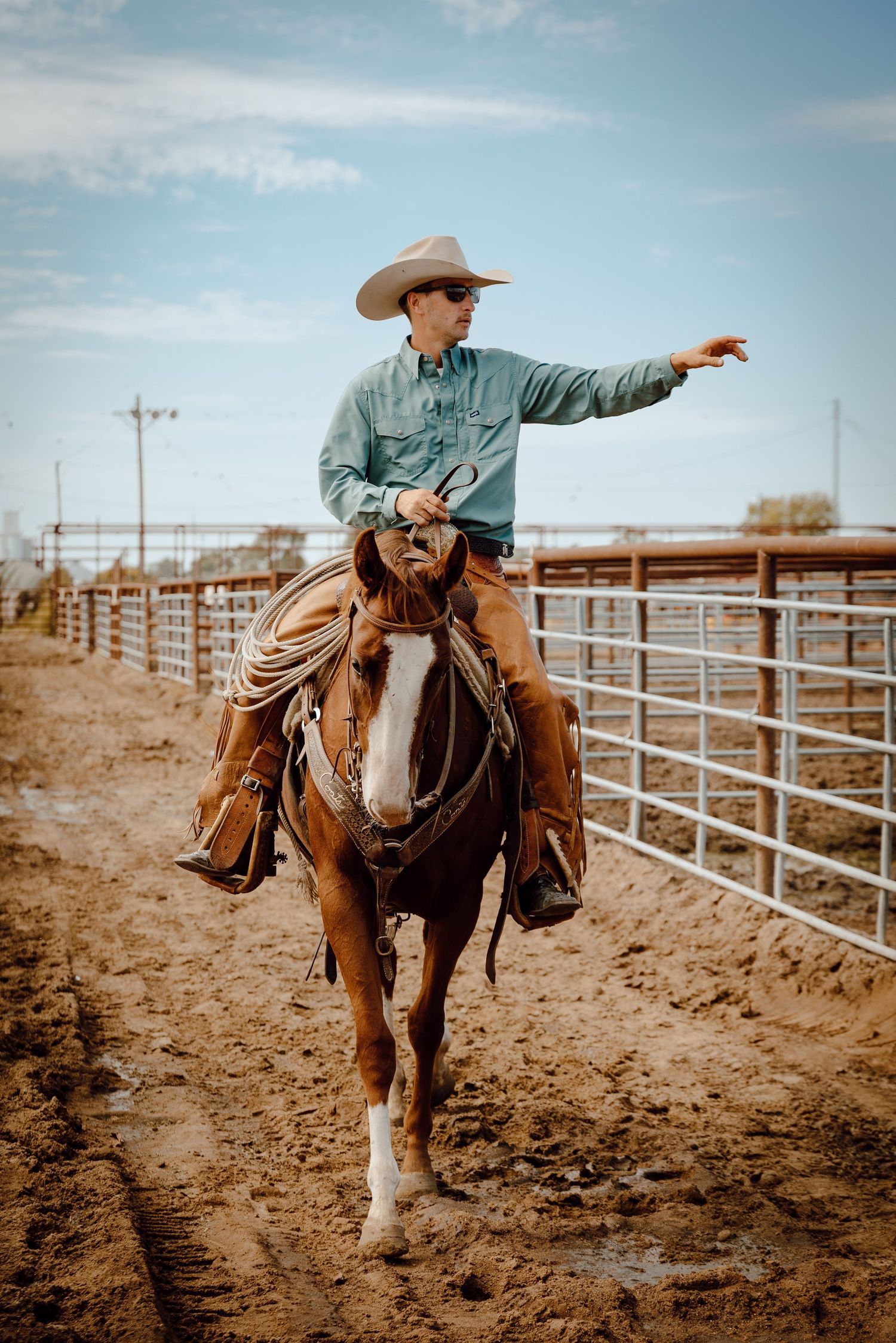 A North Platte, Nebraska lifestyle session cowboy riding his horse through dusty corral with metal fencing.