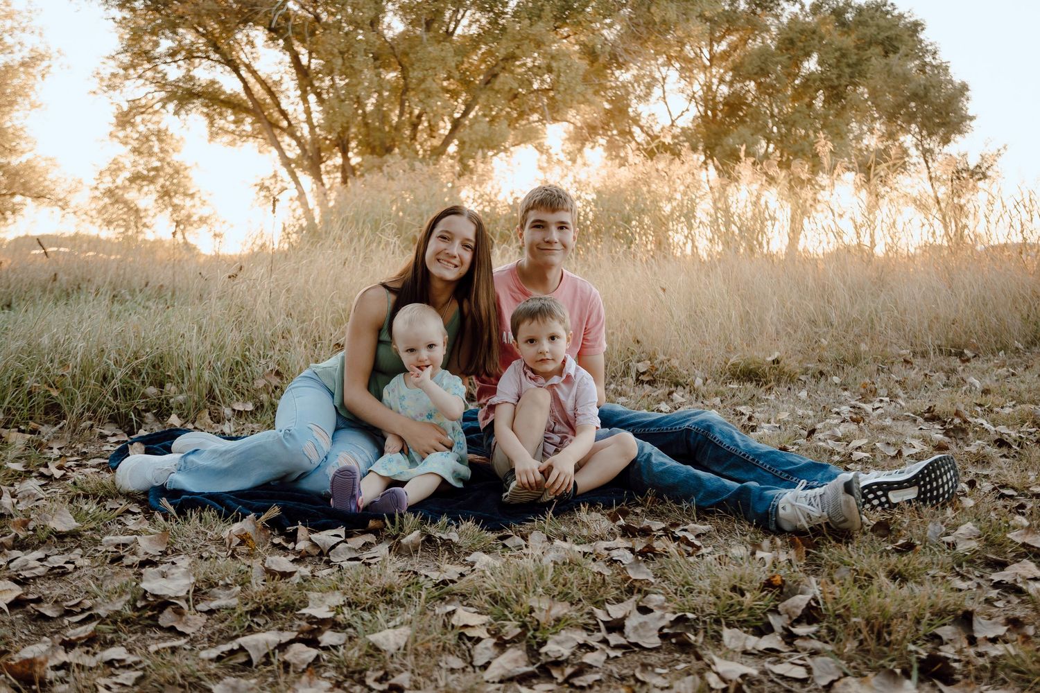 A Paxton, Nebraska lifestyle family session siblings sitting together on a blue blanket among fallen leaves during golden hour.