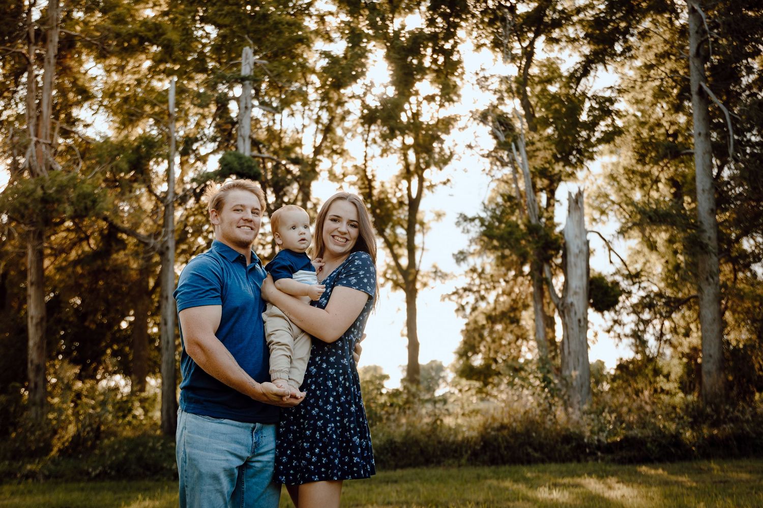 A North Platte, Nebraska lifestyle family session family shares a moment together in a sunlit wooded area.