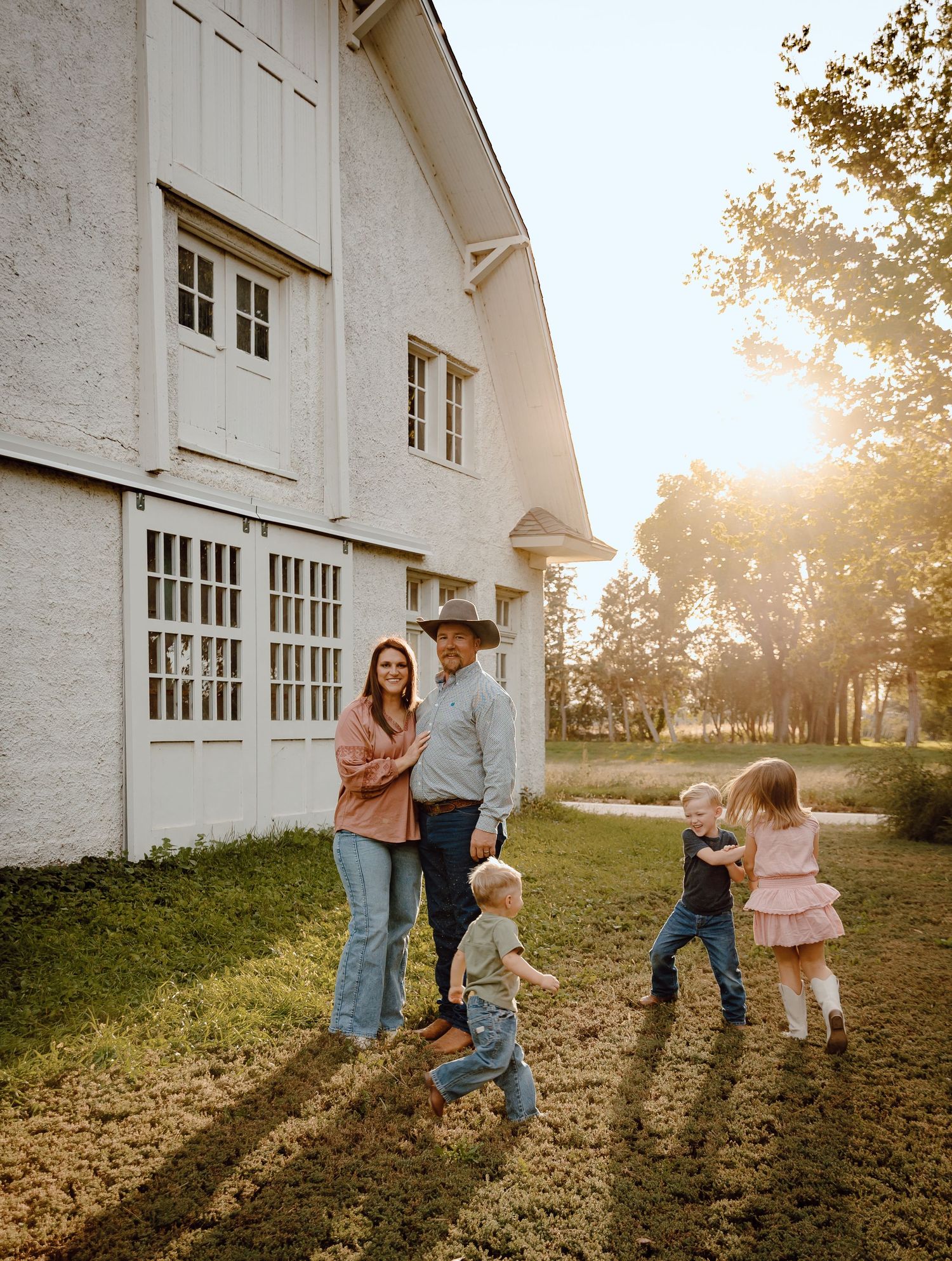 A North Platte, Nebraska lifestyle family session family enjoys a playful moment together in front of a white barn at sunset.