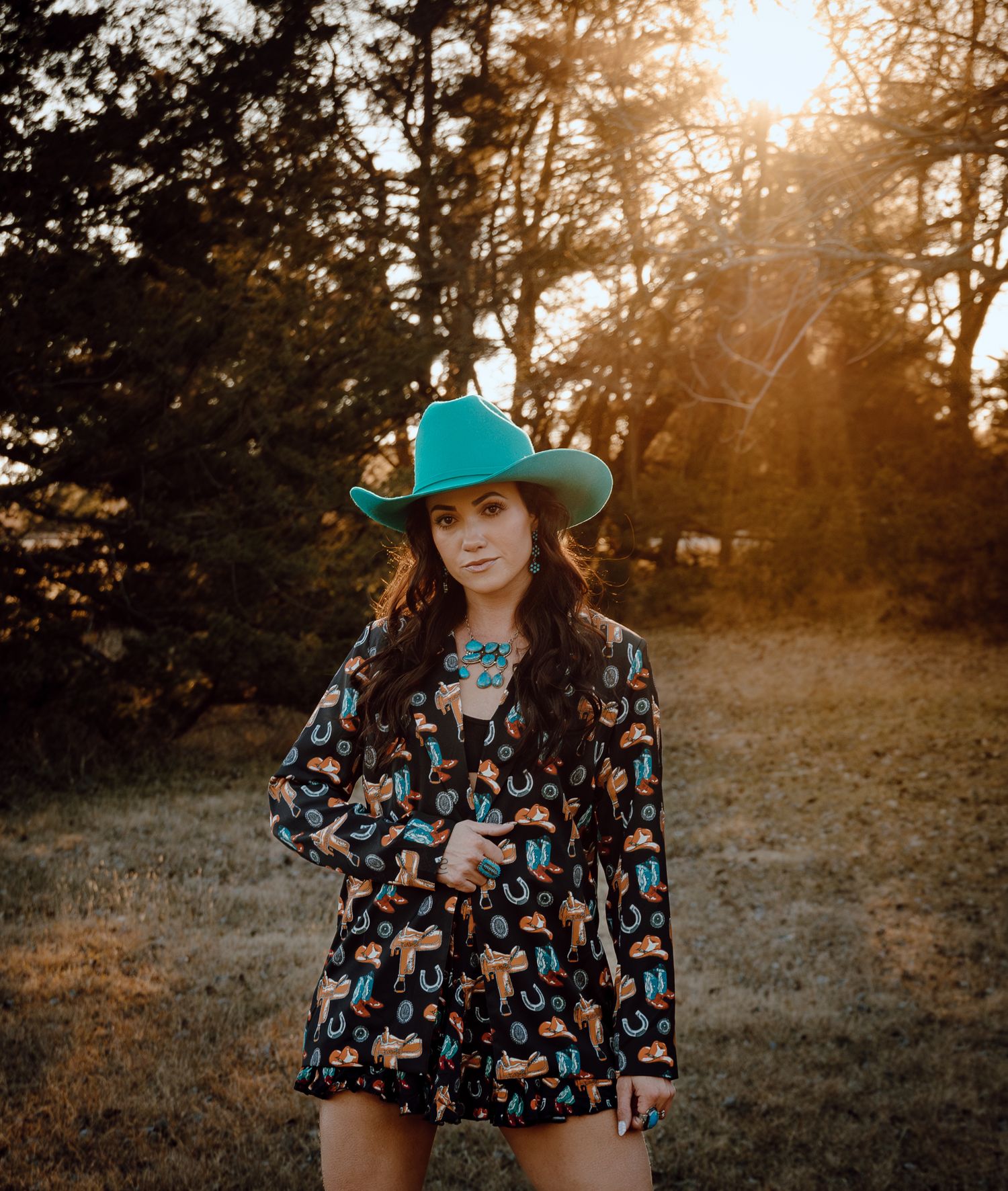A North Platte, Nebraska lifestyle session woman in a turquoise cowboy hat and pattern dress poses at sunset.