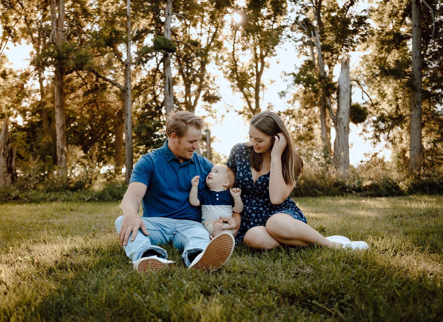A North Platte, Nebraska lifestyle family session family sits together on grass during golden hour, enjoying a tender moment outdoors.
