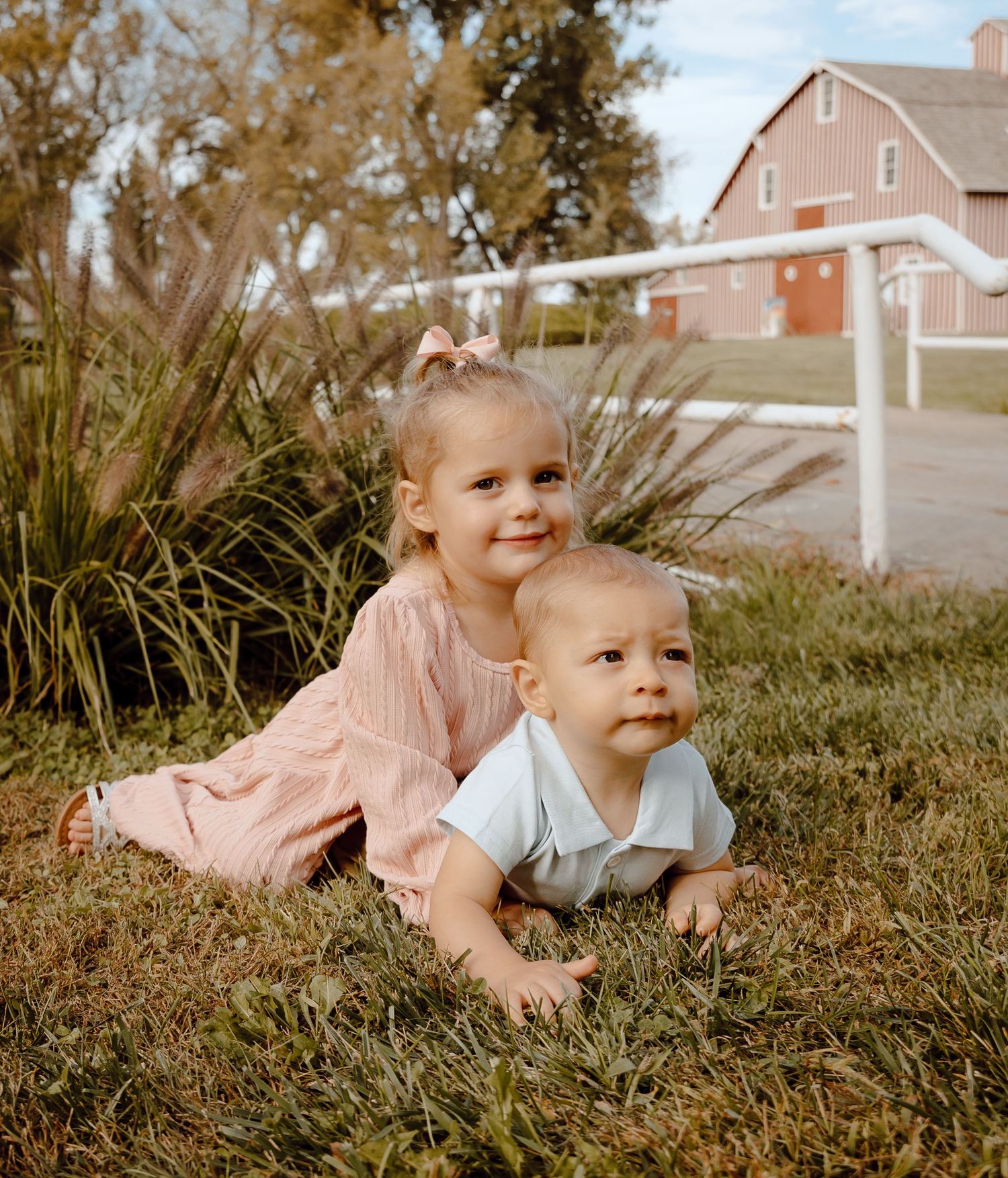 A North Platte, Nebraska lifestyle family session siblings lay together on green grass in matching outfits on a warm sunny day.