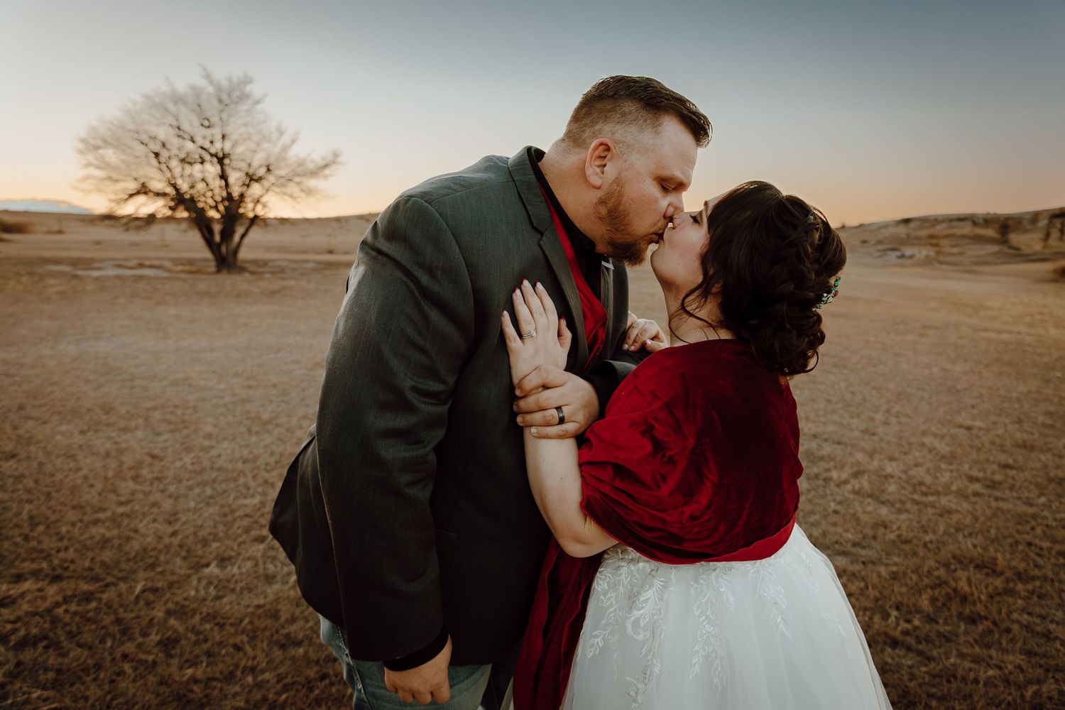 A Sidney, Nebraska lifestyle session couple shares intimate moments in a field during sunset on their wedding day.