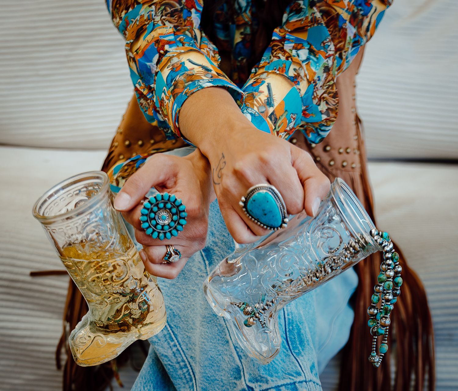 A North Platte, Nebraska lifestyle brand session woman's hands wearing turquoise jewelry holding boot shaped wine glasses.