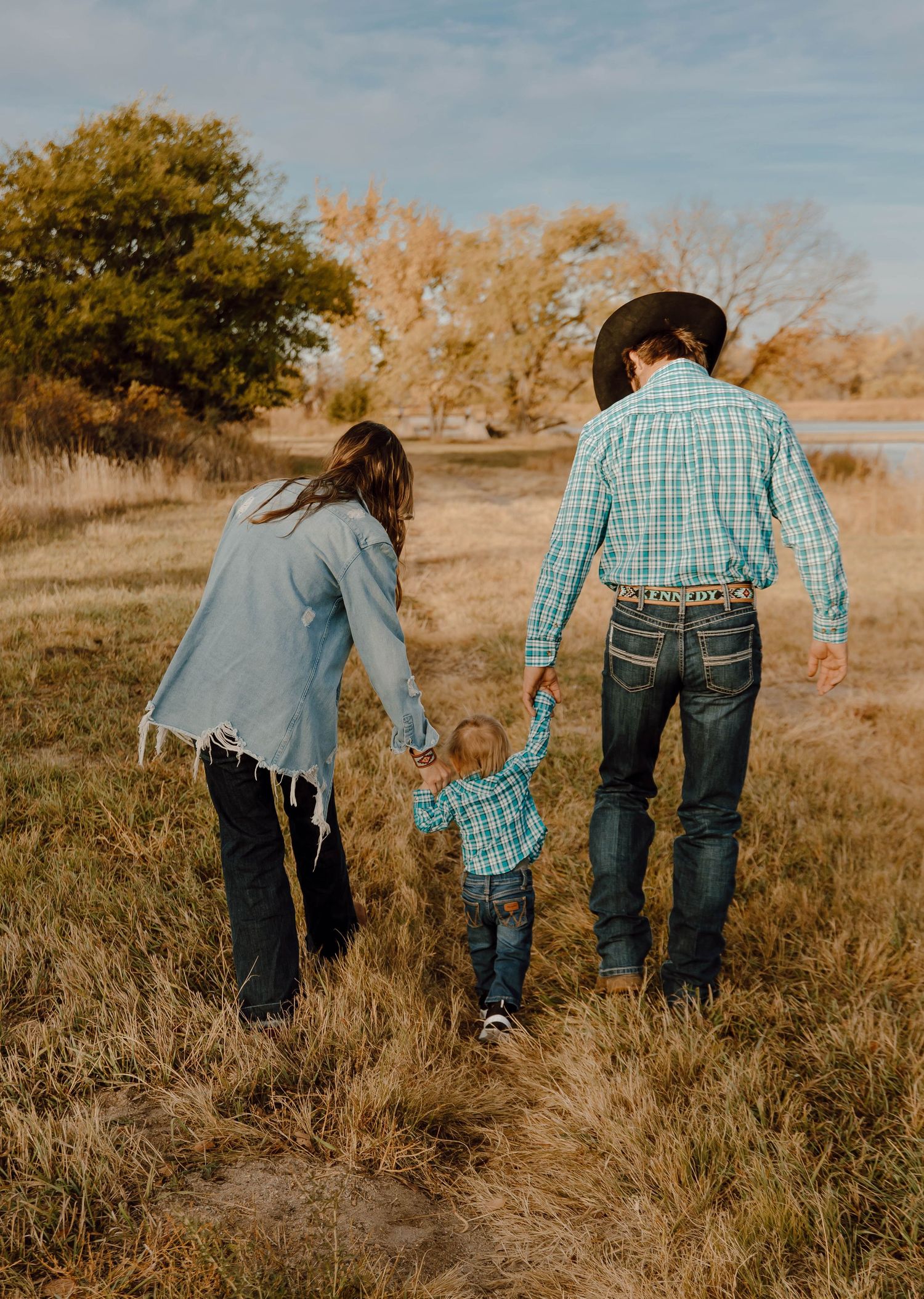 A Sutherland, Nebraska lifestyle family session family walking through tall autumn grass wearing coordinated blue and plaid outfits.