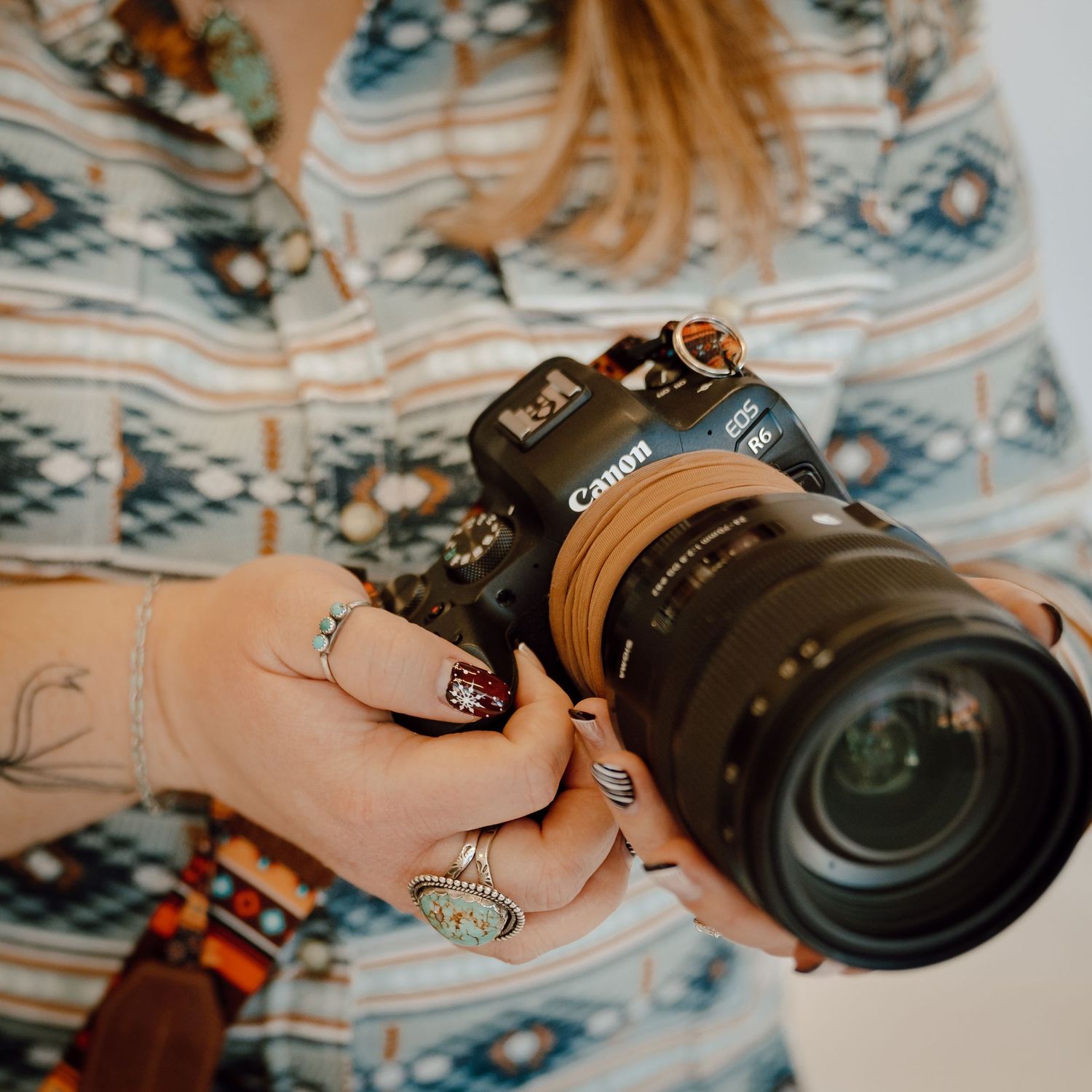 A North Platte, Nebraska lifestyle photographer holds a Canon camera with lens against a patterned background.