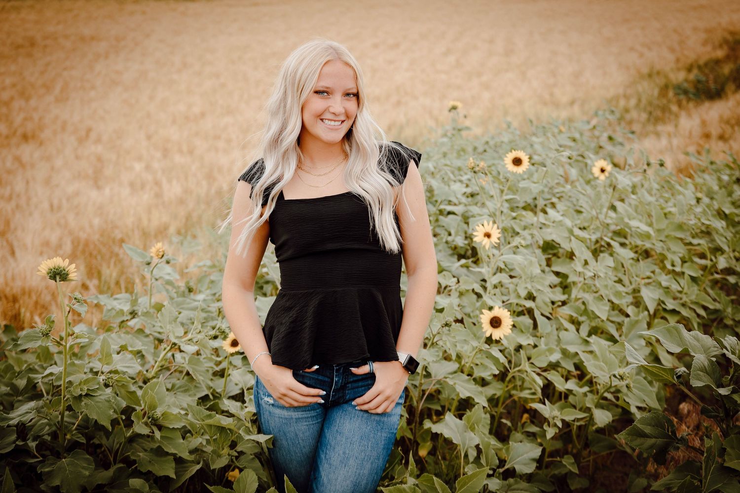 A Chappell, Nebraska lifestyle senior session girl in a black top and jeans posing among bright yellow blooms.