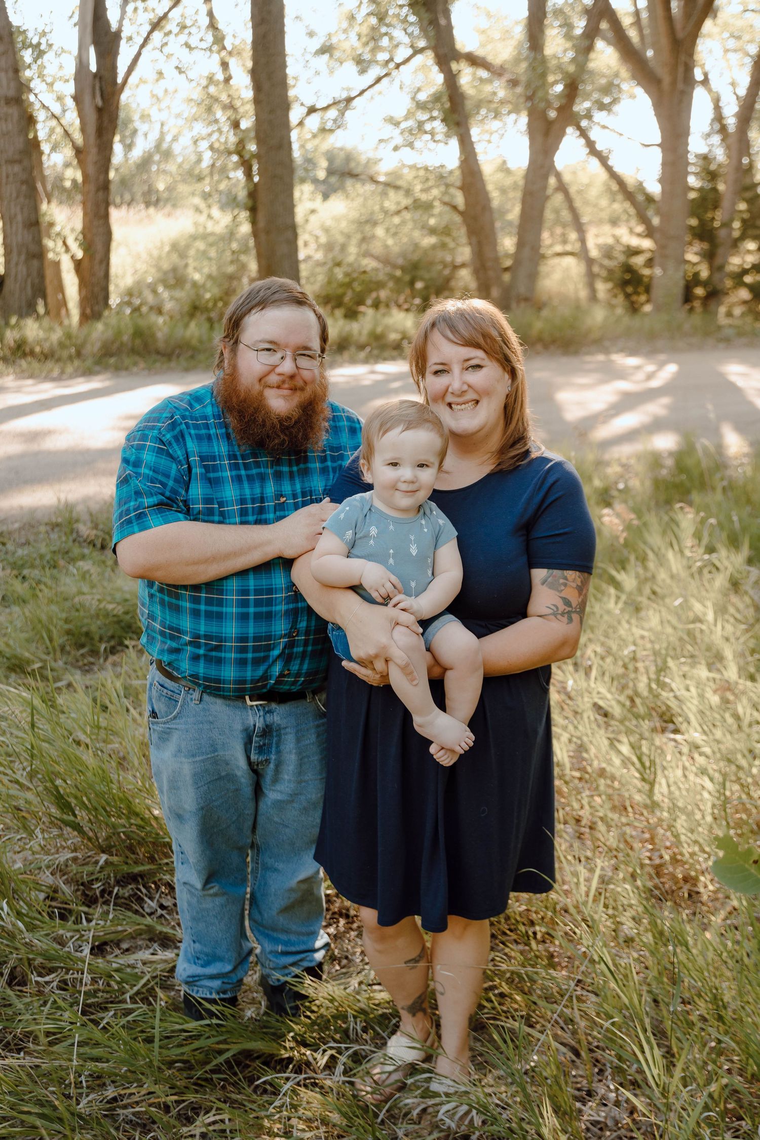 A Sutherland, Nebraska lifestyle family session family of three poses together in a sunlit wooded area.