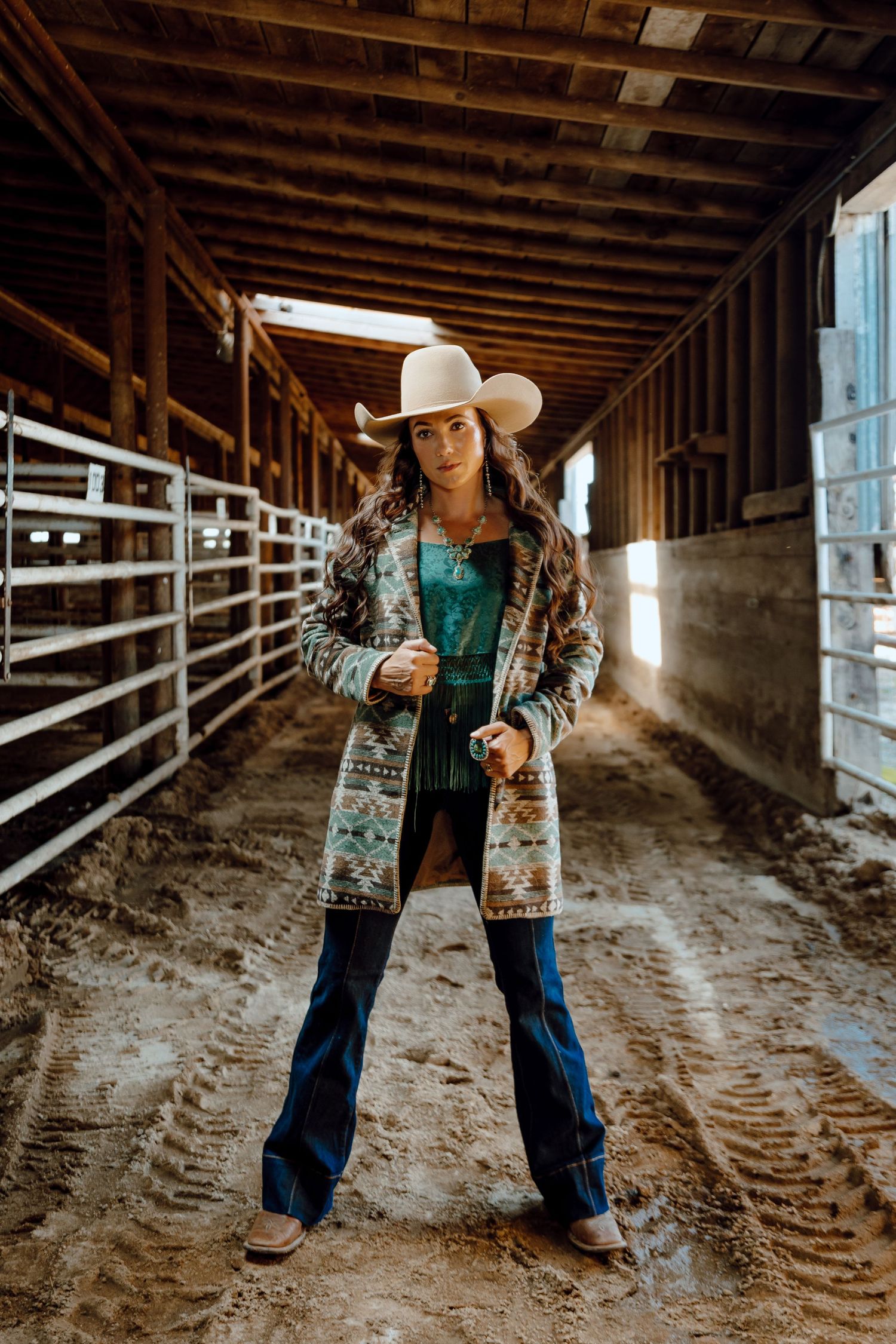 A North Platte, Nebraska lifestyle session woman wearing a patterned cardigan and jeans poses at the stockyard.