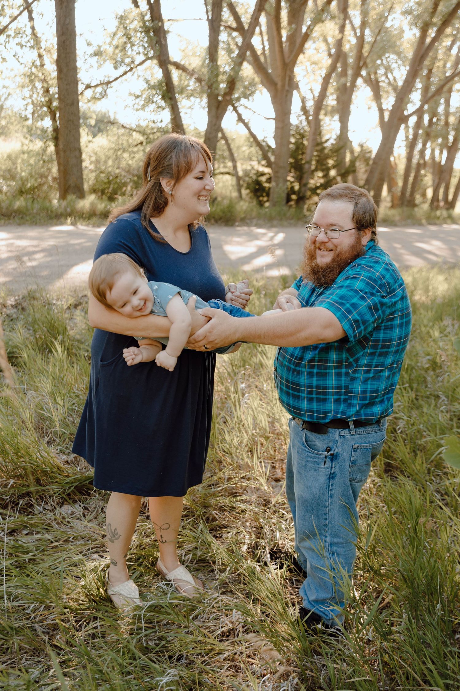 A Sutherland, Nebraska lifestyle family session family dancing and embracing in a sunlit wooded area with tall grass.