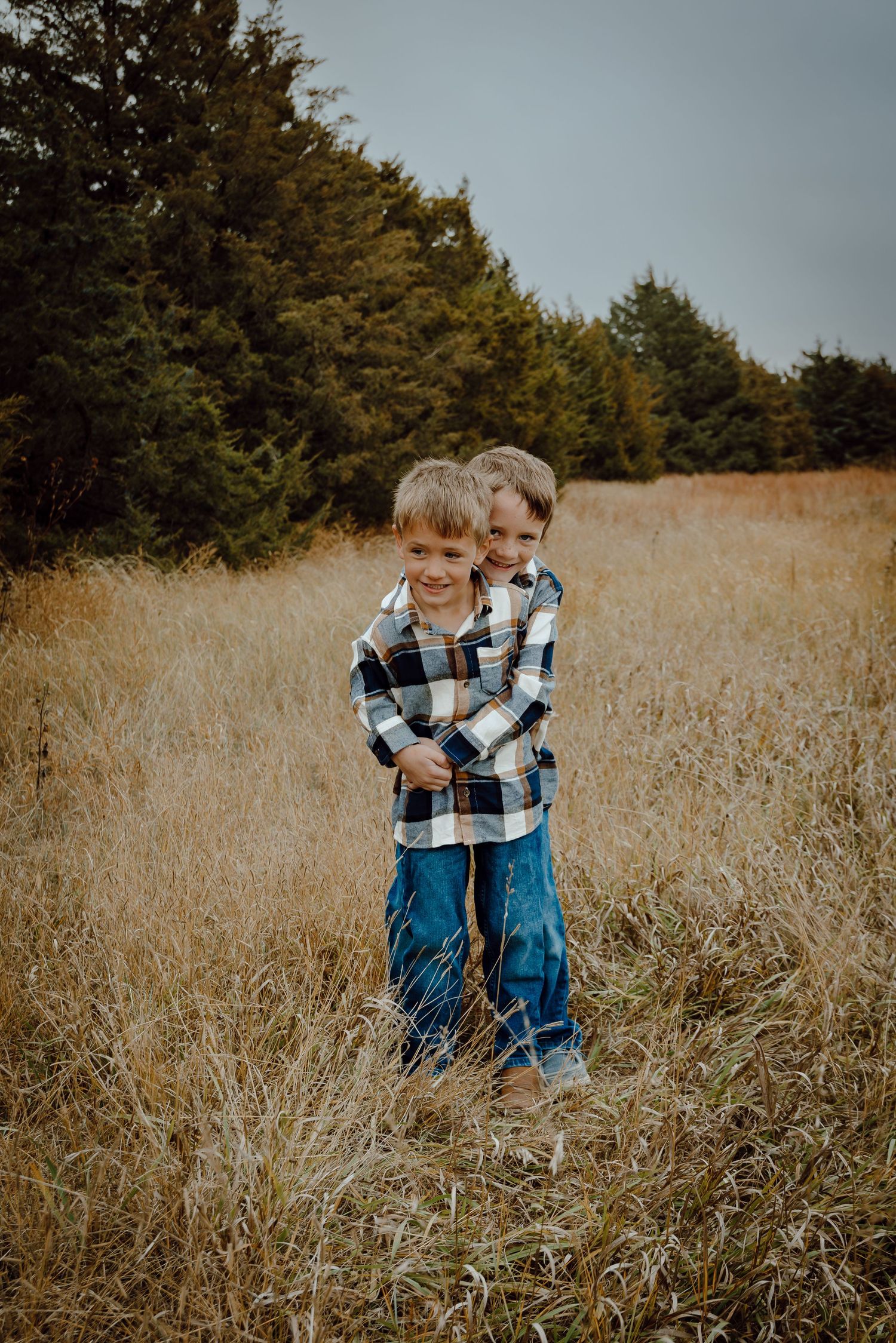 A Sutherland, Nebraska lifestyle family session brothers in a plaid flannel shirts and jeans hugging in a golden autumn field.