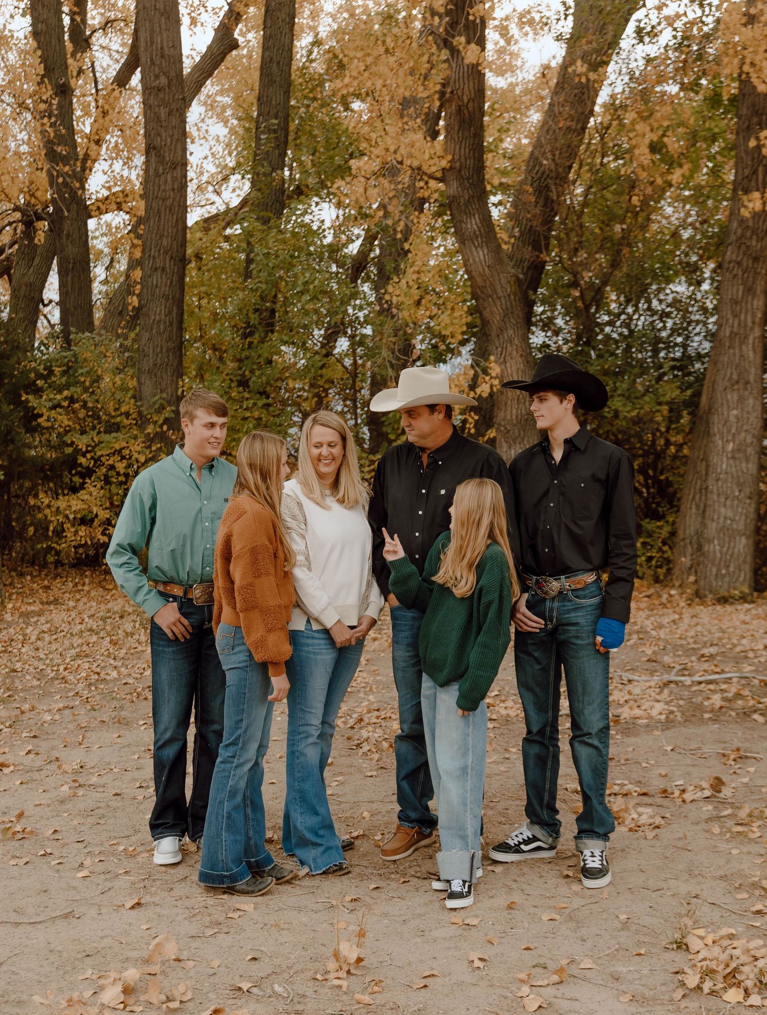 A Sutherland, Nebraska lifestyle family session family standing together in casual western wear with fallen leaves on the ground.