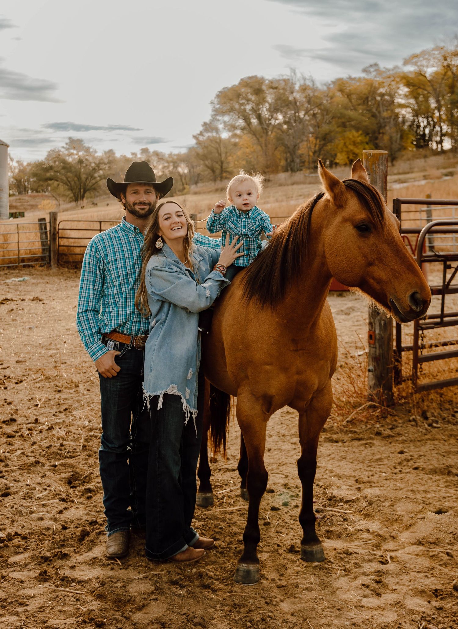 A Sutherland, Nebraska lifestyle family session family standing with their brown horse next to a rustic corral fence.