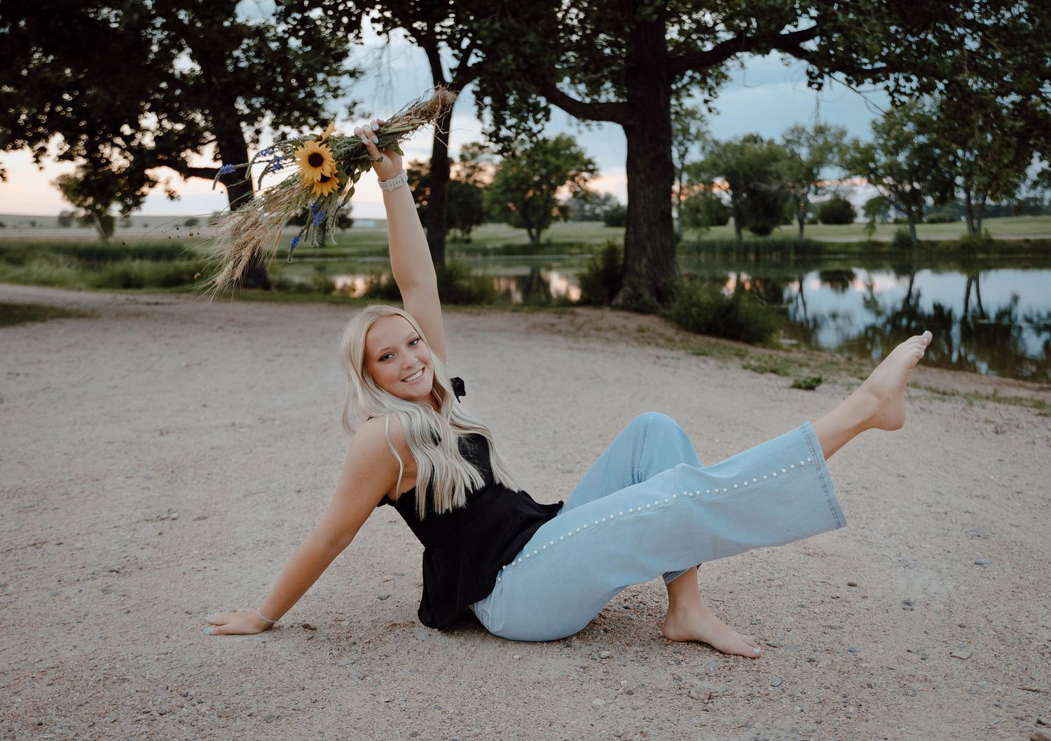 A Chappell, Nebraska lifestyle senior session girl poses at the lake with soft natural lighting holding a wildflower bouquet.