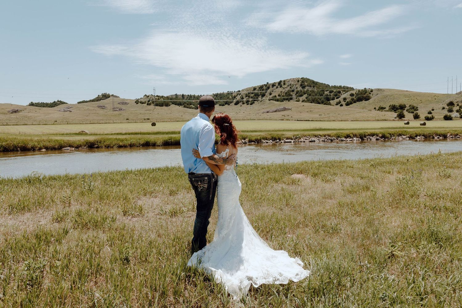 A North Platte, Nebraska lifestyle session couple embraces in scenic prairie landscape with rolling hills and blue sky on their wedding day.