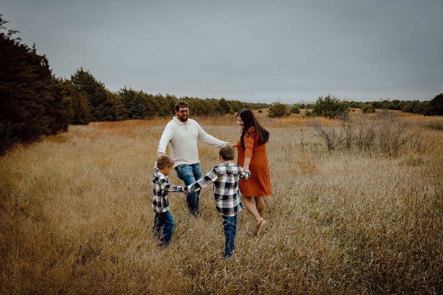 A Sutherland, Nebraska lifestyle family session family walks together through a golden autumn field  holding hands.