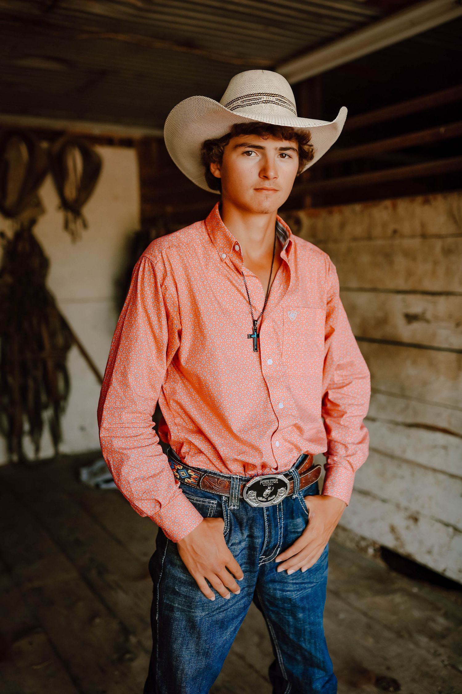 A Curtis, Nebraska lifestyle senior session boy in a pink button-down shirt, jeans, and cowboy hat in a rustic setting.