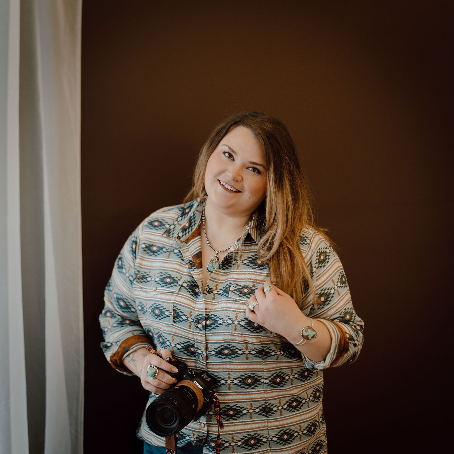 A North Platte, Nebraska lifestyle photographer in a western style shirt poses against a brown background.
