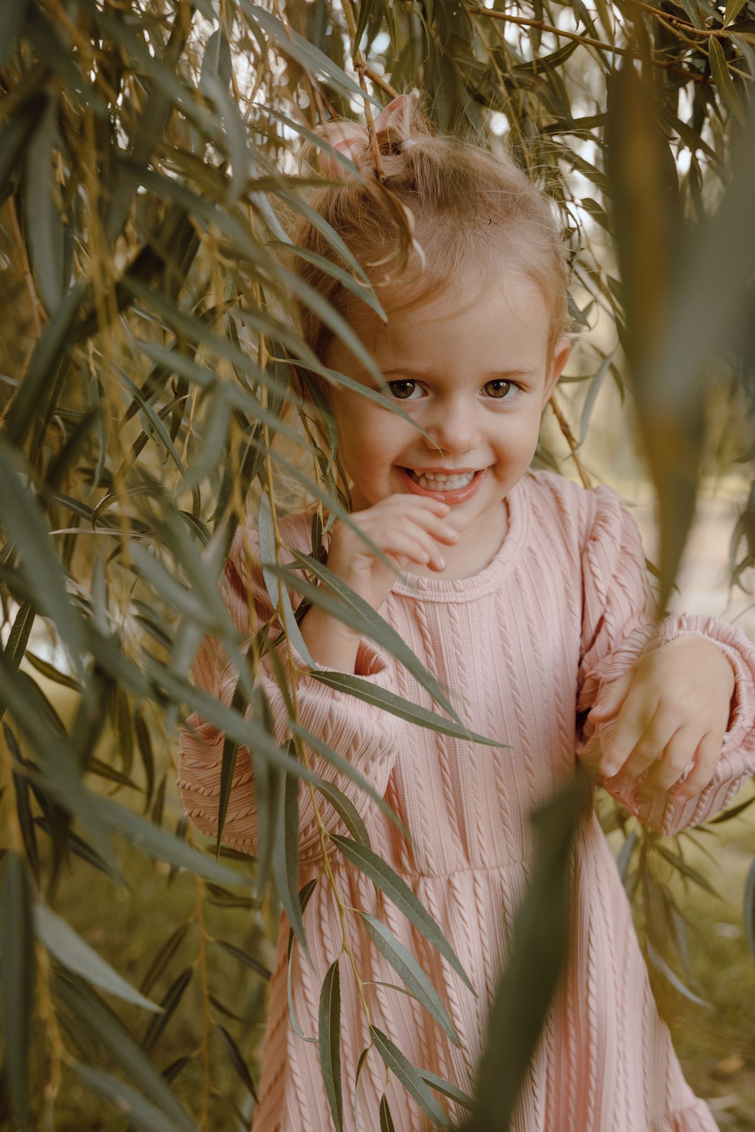 A North Platte, Nebraska lifestyle family session girl peeks playfully through willow tree branches.