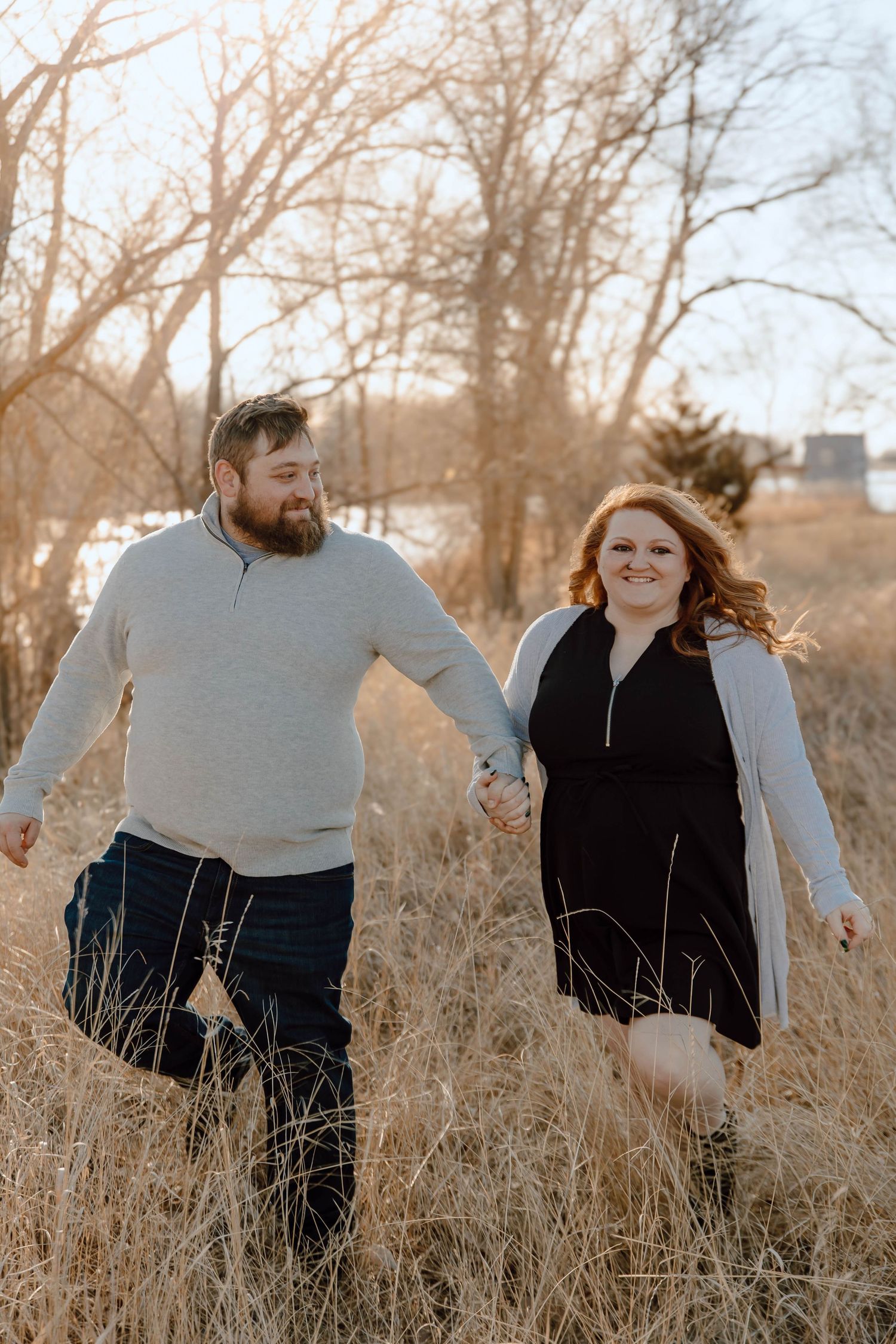 A North Platte, Nebraska engagement session couple walks together in a golden field of tall grass during sunset.