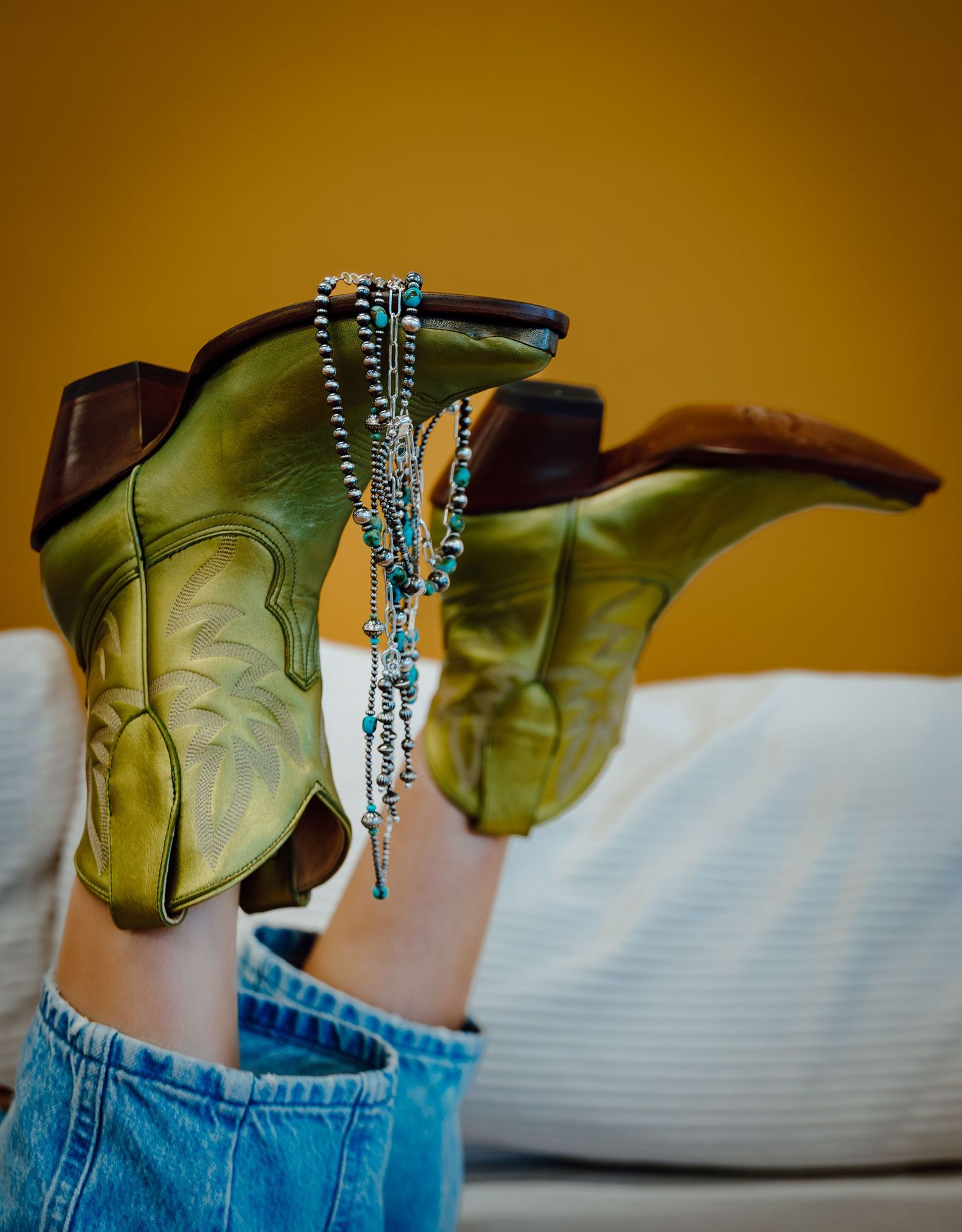 A North Platte, Nebraska lifestyle brand session green boots with silver jewelry displayed against a warm orange background.