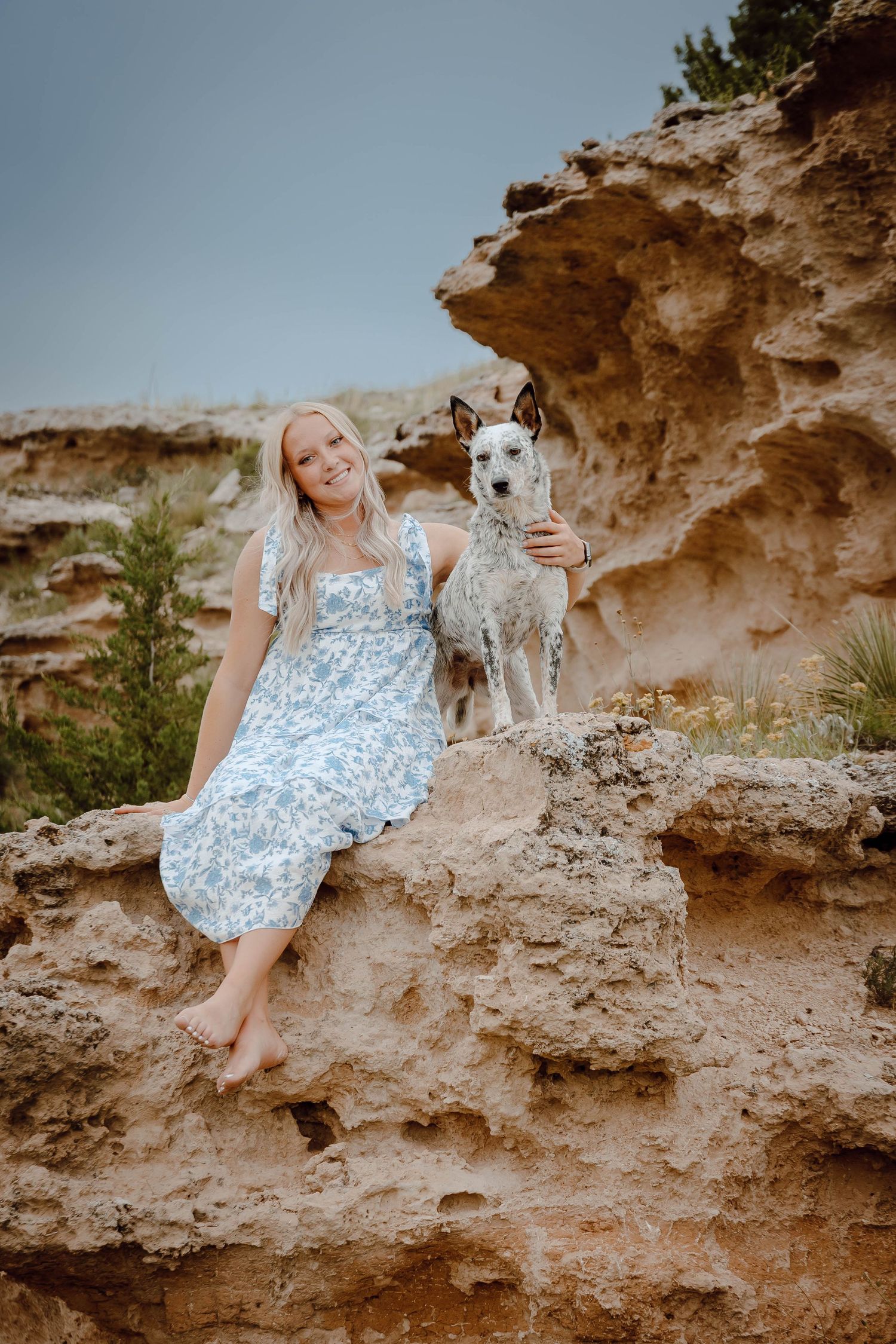 A Oshkosh, Nebraska lifestyle senior session girl sits on rocky terrain with a white and gray dog.
